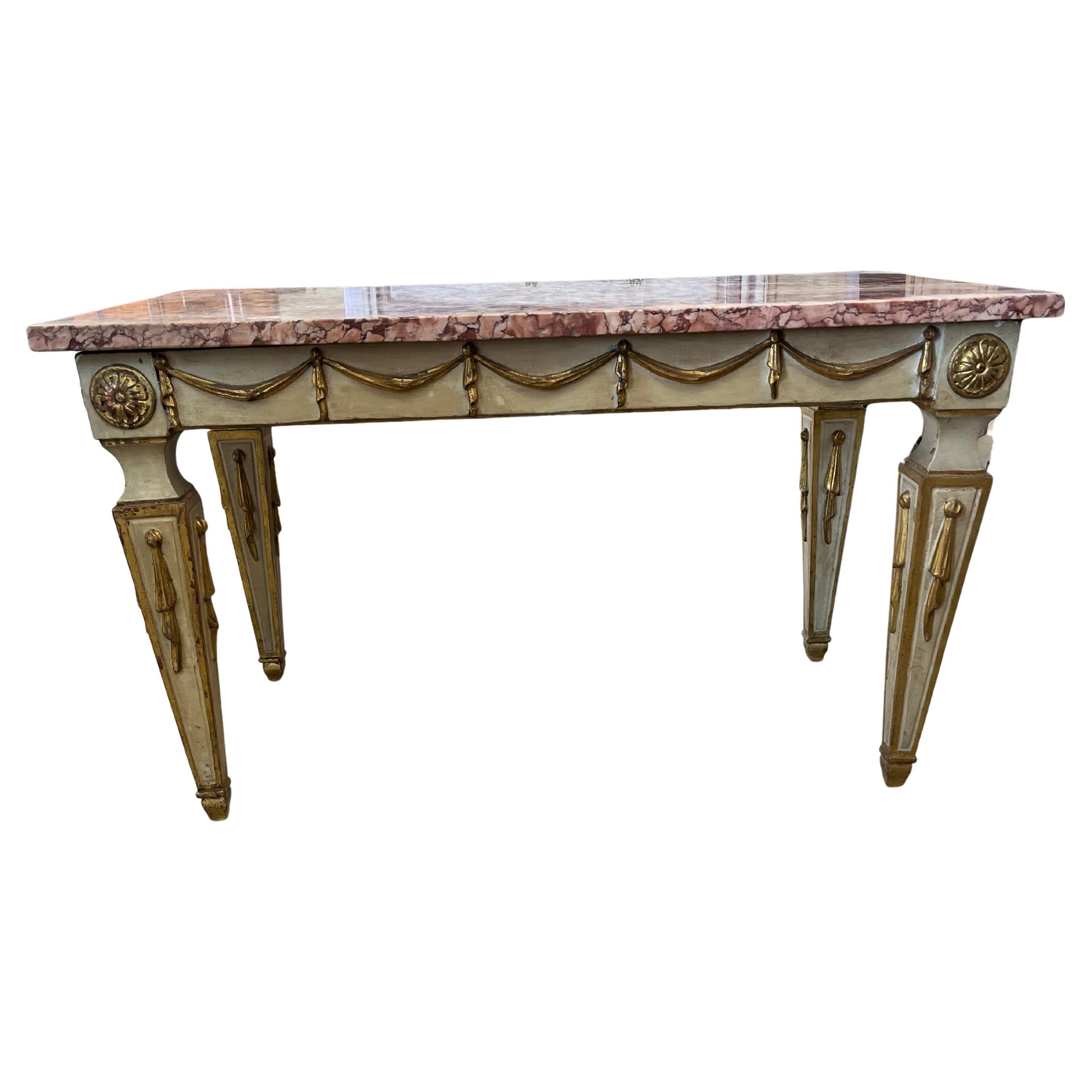 Coffee table hand-made in Italy in the early 1900s following the lines of the neoclassical style. The table is painted and adorned with applied and gold-leafed hand-carvings . The edges of the legs are also decorated with gold leaf. The legs are
