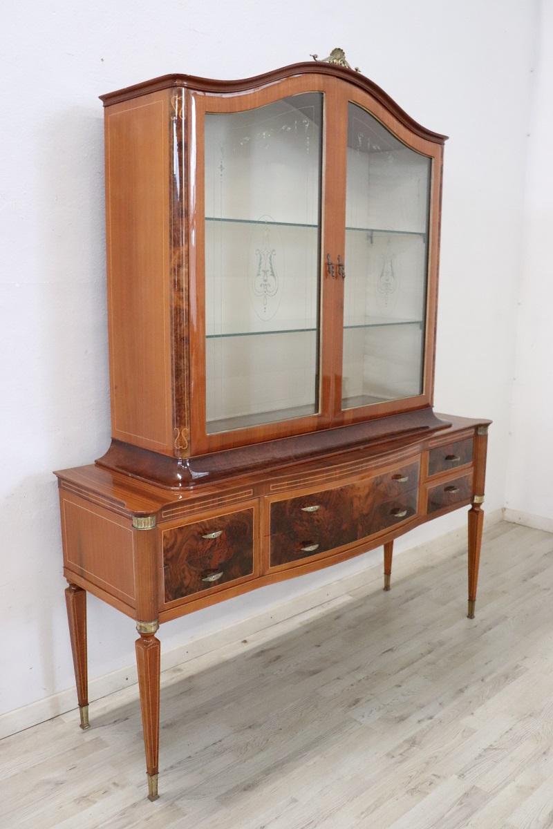 Esta vitrina de estilo neoclásico italiano expresa elegancia y refinamiento en cada detalle. Fabricada a mediados del siglo XX en chapa de nogal con elegantes detalles en brezo y arce. Su estructura se compone de dos cuerpos que pueden dividirse