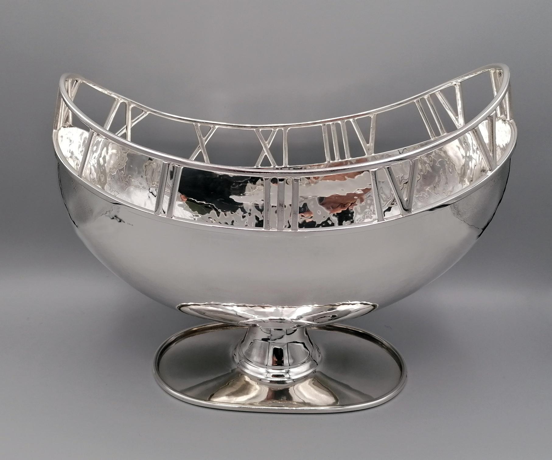 800 silver oval centerpiece with base. The body was made by hammering the silver sheet by hand and then welded on a foot which is also oval and with a raised edge. 
In the upper edge, Roman numerals have been cutout of silver and then welded with