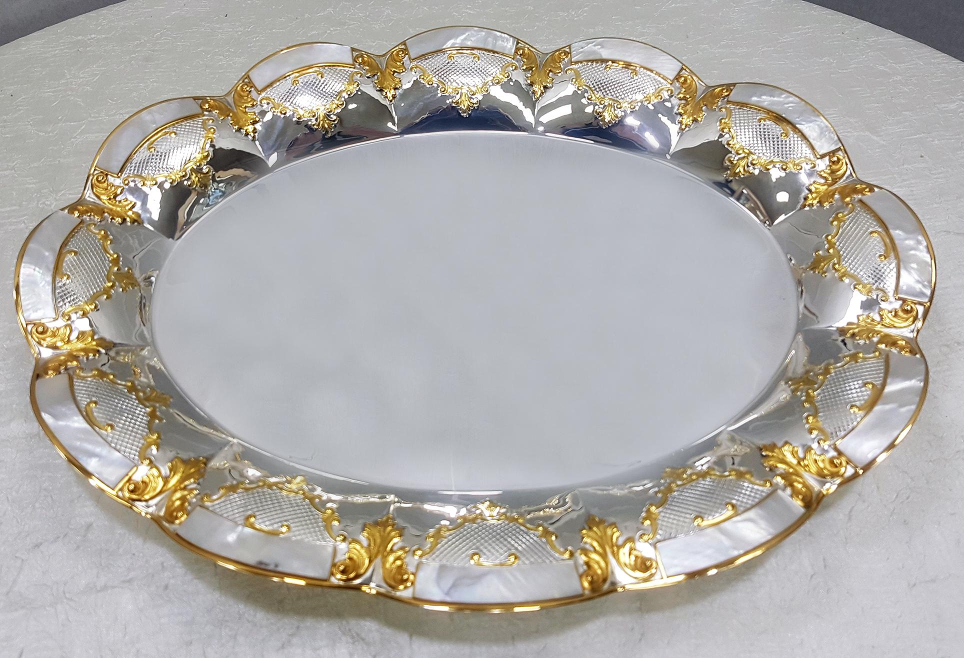 Solid silver 800 oval centerpiece on gilded feet with mother of pearl inserts and gilded details.
Completely handmade, ceased and embossed, it has a wavy oval shape.
Made in Italy.

  