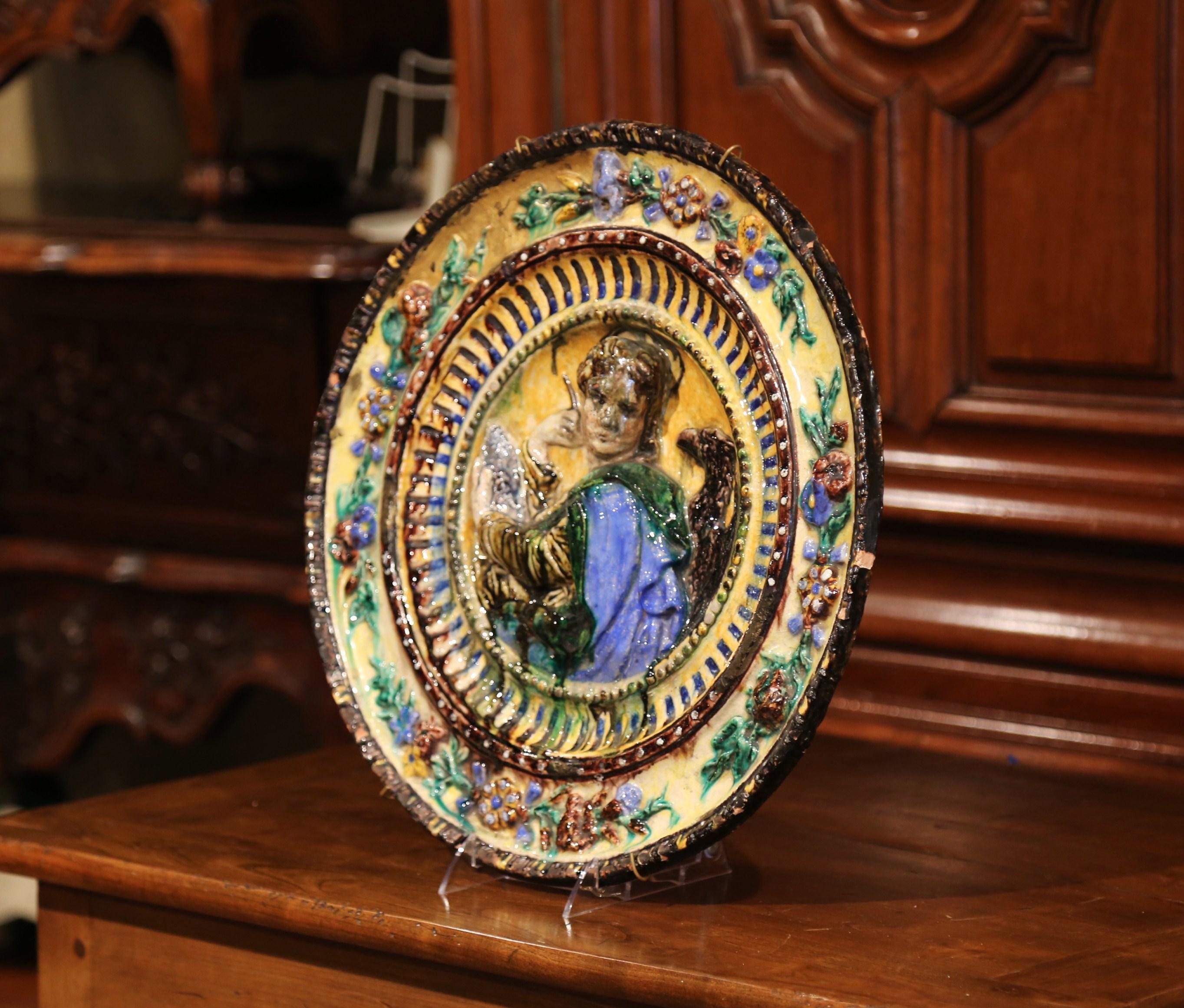 Decorate a wall with this antique and colorful barbotine platter; crafted in Italy, circa 1920, the large charger features Saint John the Evangelist holding a pen and writing a book, with an eagle standing on the side, symbolizing the elevation of