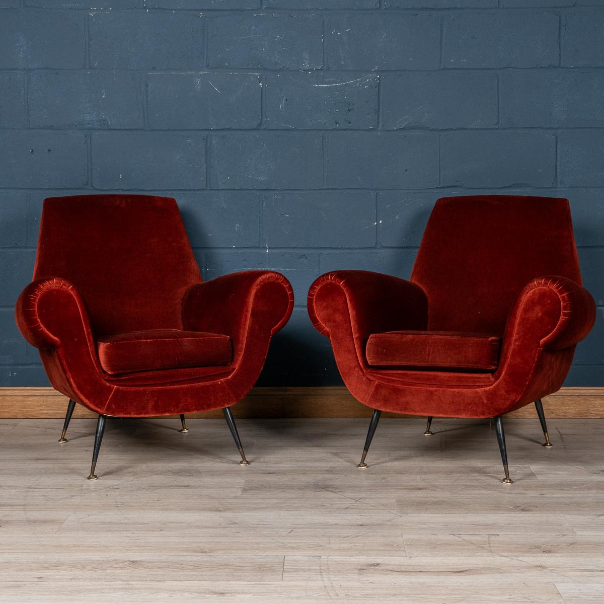 A lovely pair of armchairs made in Italy in the middle part of the 20th century. These armchairs have been upholstered in a sumptuous crimson velvet, the striking mid century design with sharp angles, tapered legs finished with brass tips fits so