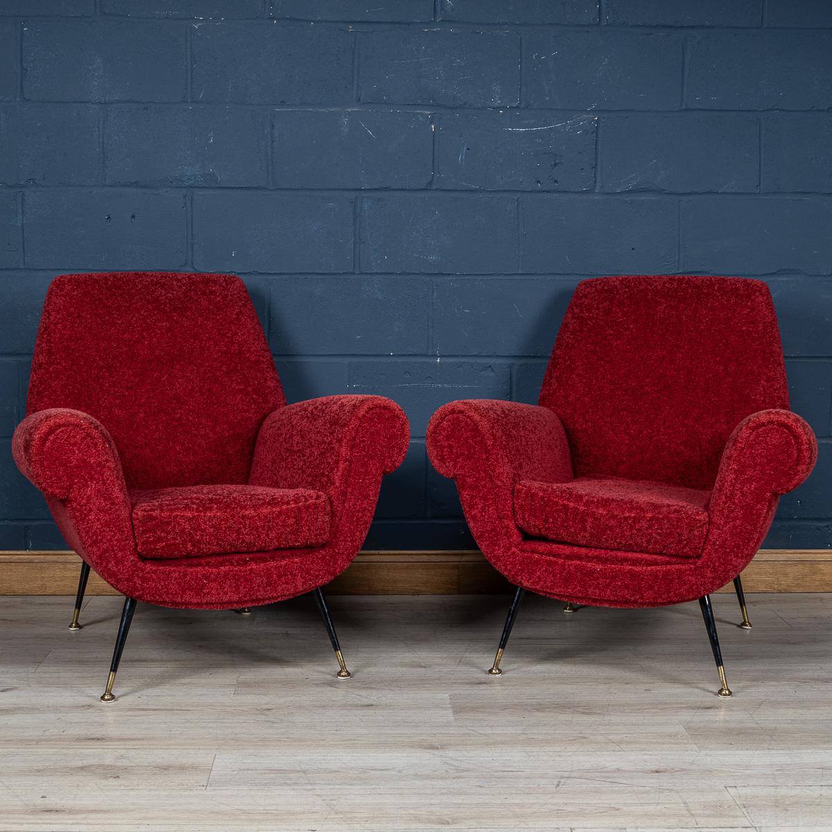 A lovely pair of armchairs made in Italy in the middle part of the 20th century. Upholstered in a luxurious crimson boucle' fabric, the armchairs embody a striking mid-century design characterised by sharp angles, tapered legs, and brass tips,