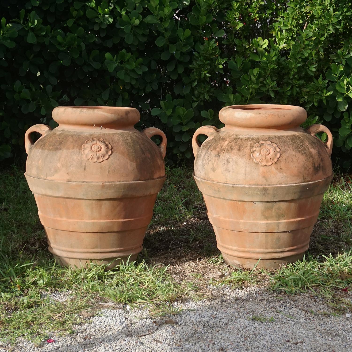 Une paire d'urnes de jardin toscanes rustiques vintage surmontées d'un lourd bord roulé, décorées de rosettes et de larges bandes autour du corps des jardinières, en bon état. Ces urnes sont fabriquées en terre cuite. Usure conforme à l'âge et à
