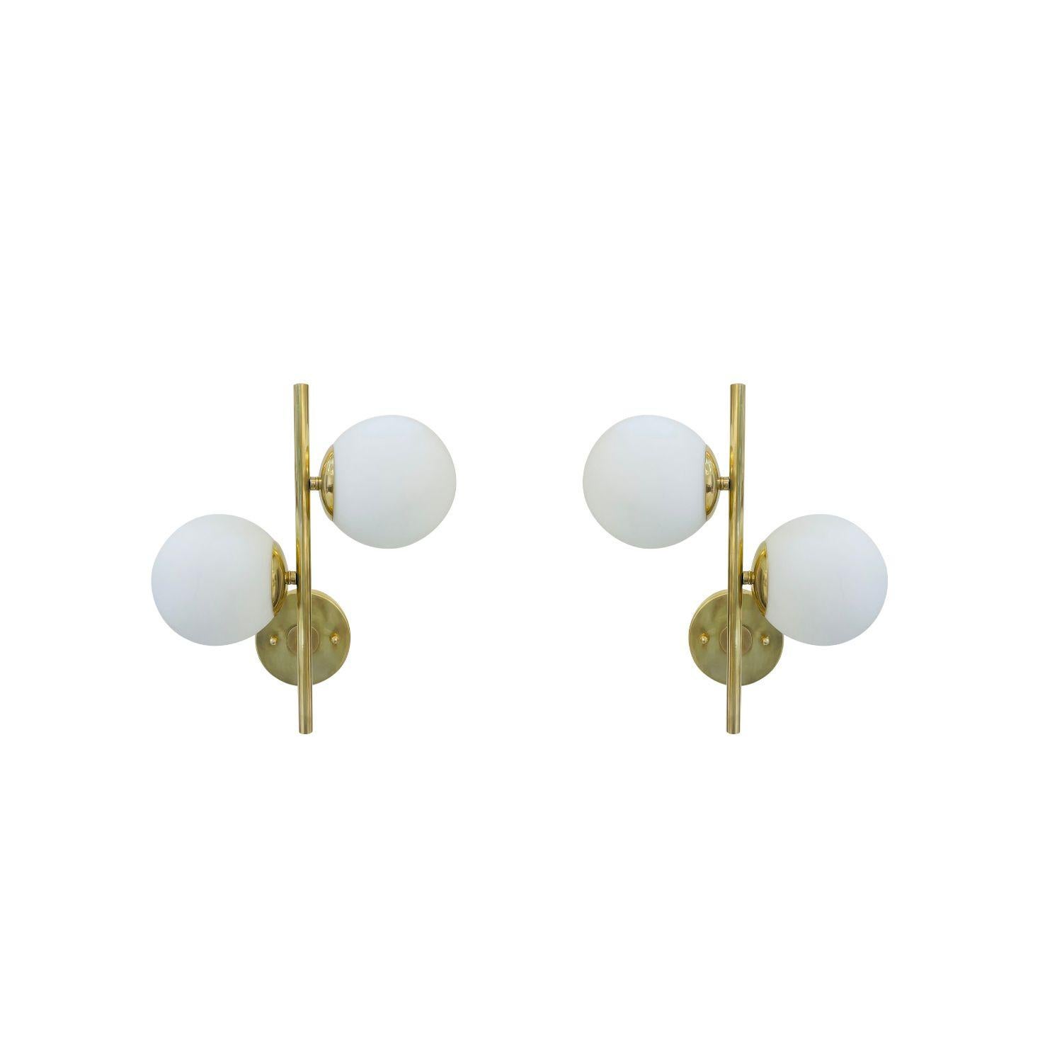 A vintage Mid-Century modern pair of Italian wall lamps made of hand crafted polished brass designed and produced by Stilnovo, in good condition. Each of the wall appliques, sconces are composed with two frosted opaline glass shades which are