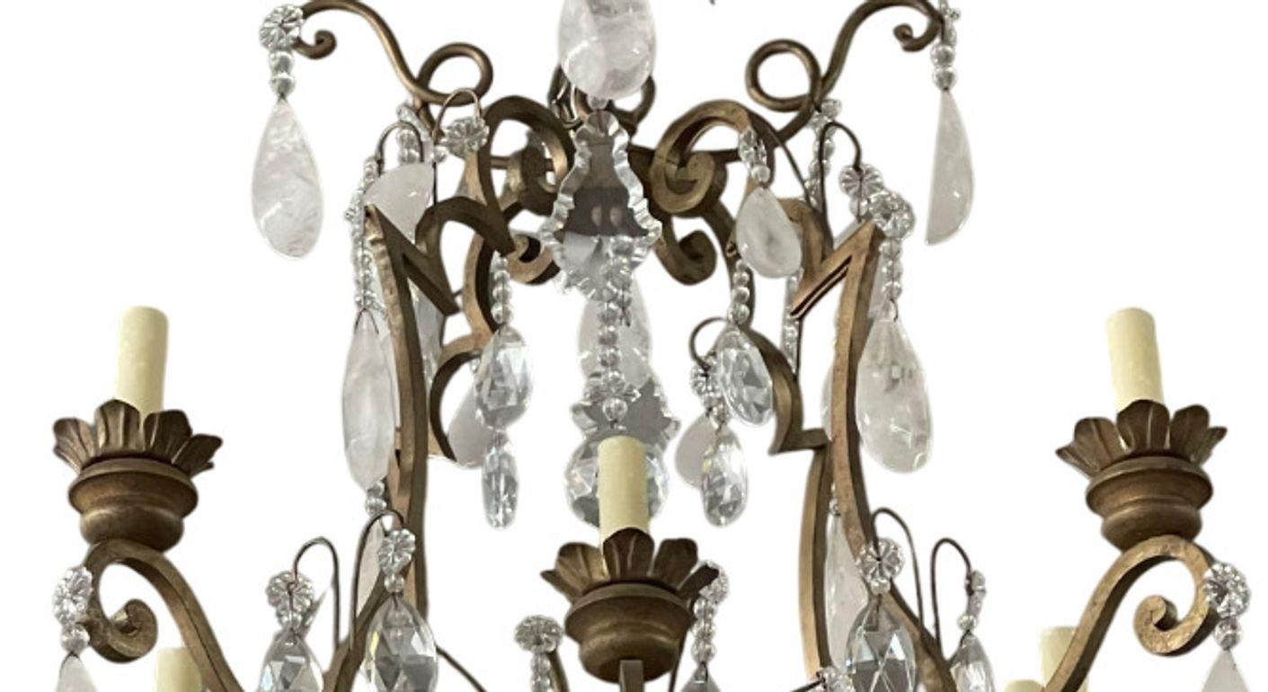 An exquisite 20th century Italian chandelier adorned with an abundance of natural rock crystal drops. This elegant fixture features eight scrolling arms with candle-style lights, all mounted on a hand-forged iron frame finished in a rich, dark gold