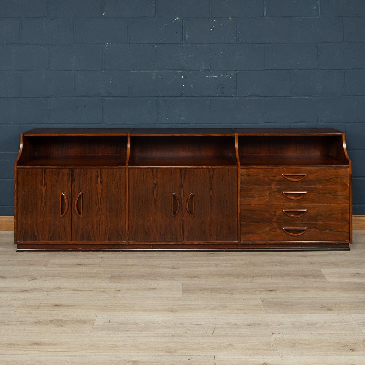 A large rosewood sideboard made in Italy around the middle of the 20th century. The sideboard consists of three sections, two with doors opening to reveal shelves for storage, the other with a bank of four drawers. The beautiful inset handles, so