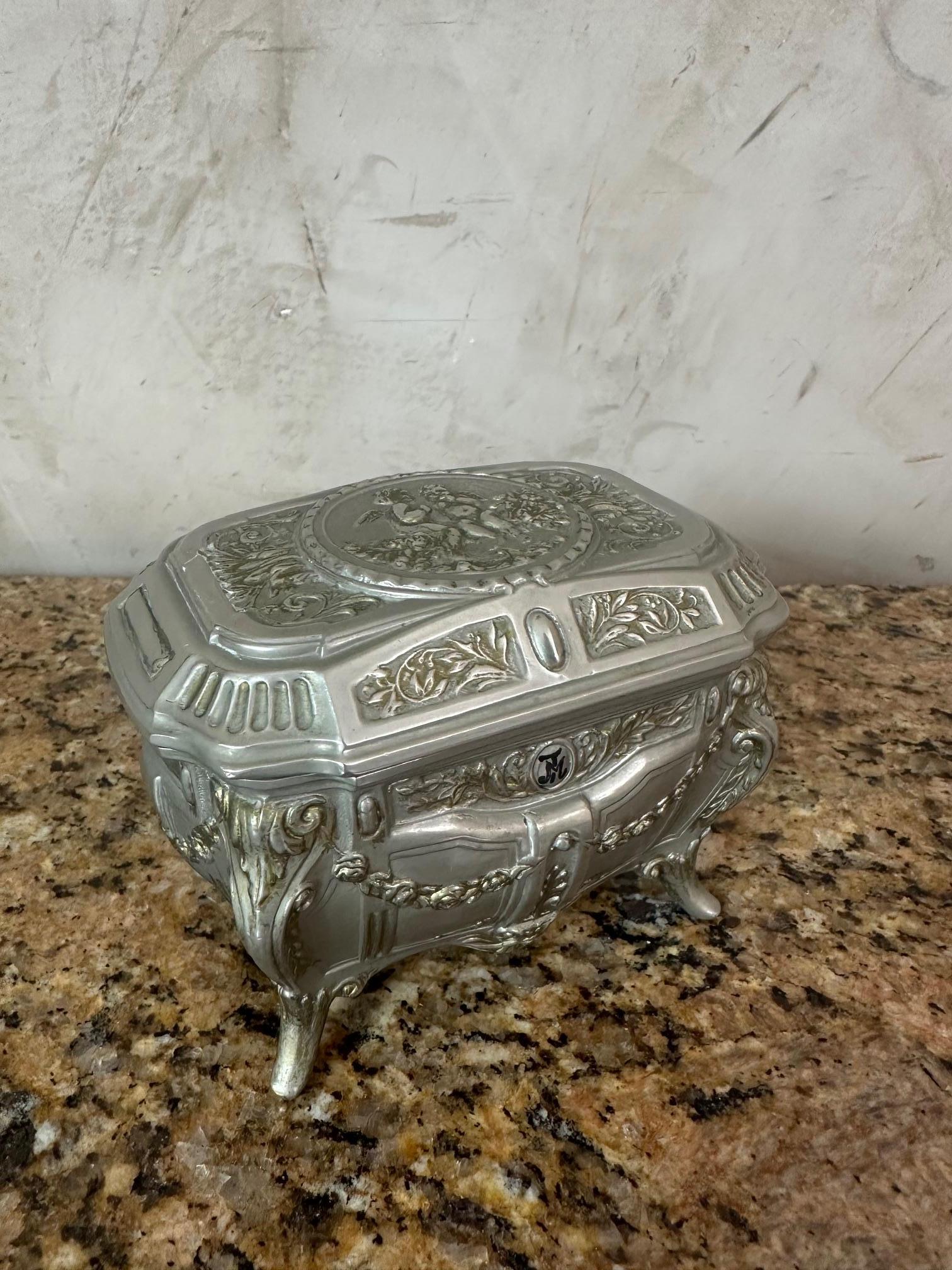 Adorable small musical box in silver-plated metal, made in Italy in the 1960s.
Its finely crafted design, adorned with floral motifs and gilded garlands, evokes the Rococo style with its curved lines and delicately shaped feet.

When the lid is