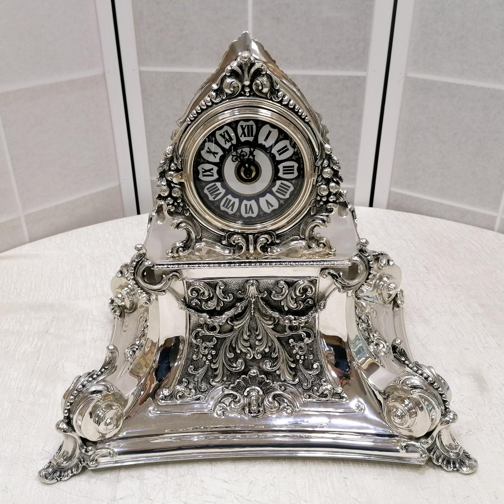 Horloge de table de style baroque italien, en tôle d'argent repoussée avec des tourbillons typiques du style baroque. Des détails moulés décorent ses quatre côtés et sa couronne.
Le cadran est en céramique émaillée et le mouvement est