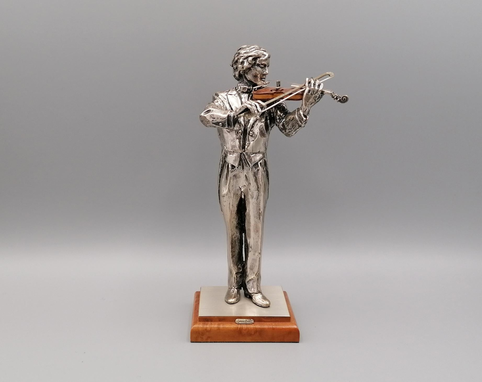 Violin player in 800 solid silver. The violin is in briar with silver details.
The violin bow is in silver.
The player and the violin are positioned on a wooden base covered in silver at the top.