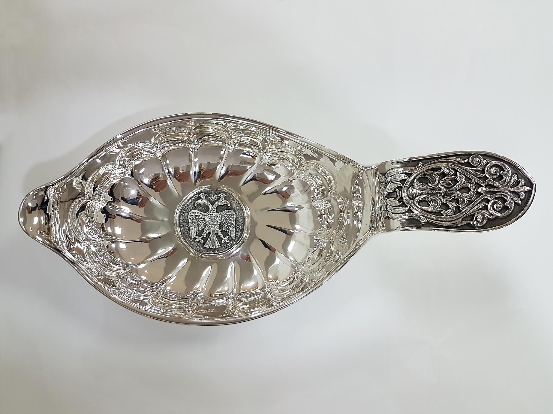 Solid 800 Silver Kovsh completely ceased and embossed by hand.
A medallion depicting a two-faced Royal eagle was placed in the centre of the bowl.
On the handle there is a frieze worked in fusion depicting volutes.

The Kovsh is a traditional