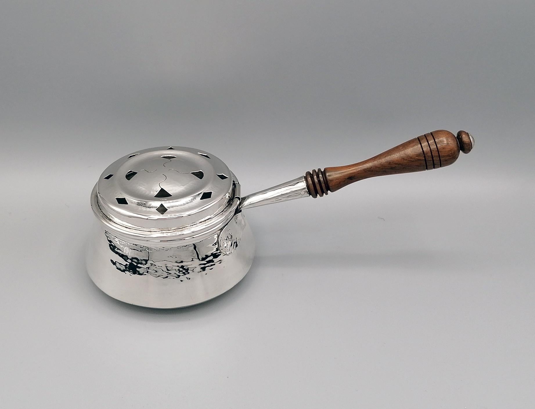 Round conical shape warmer in 800 solid silver. The silver sheet is hammered.
The hinged lid has been pierced by hand with holes in the shape of a rhombus and triangle.
The wooden handle is fixed to the body of the warmer with a silver support