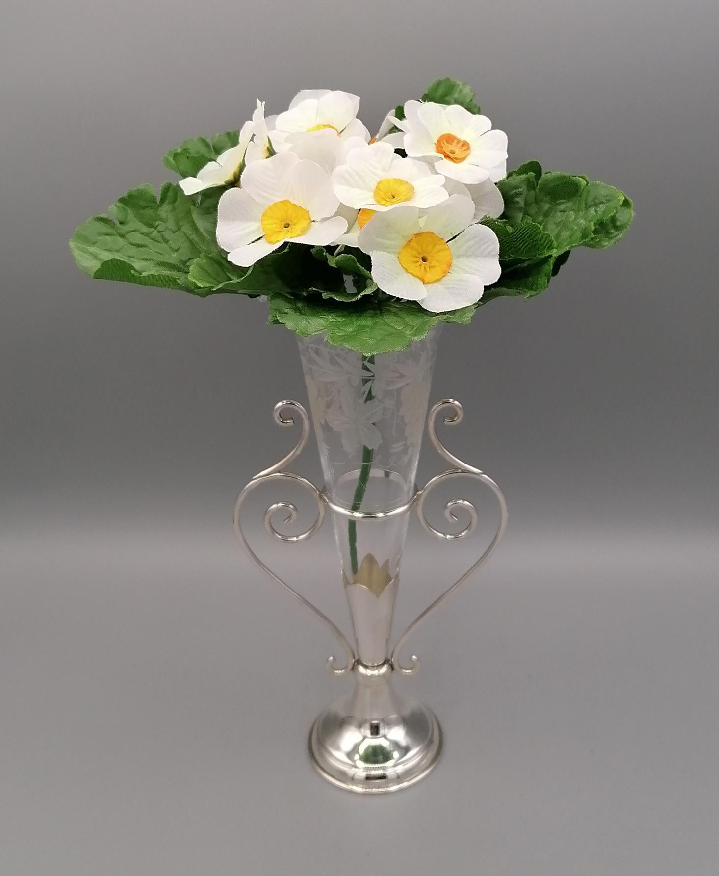 Vase aus Sterlingsilber mit rundem Sockel und Drahtgriffen. Über dem Sockel ist ein zackiger, kegelförmiger Vasenhalter angebracht. Die Hände in Silberfäden zeichnen Schriftrollen als Dekoration.
Der Blumenhalter aus Kristall ist konisch und