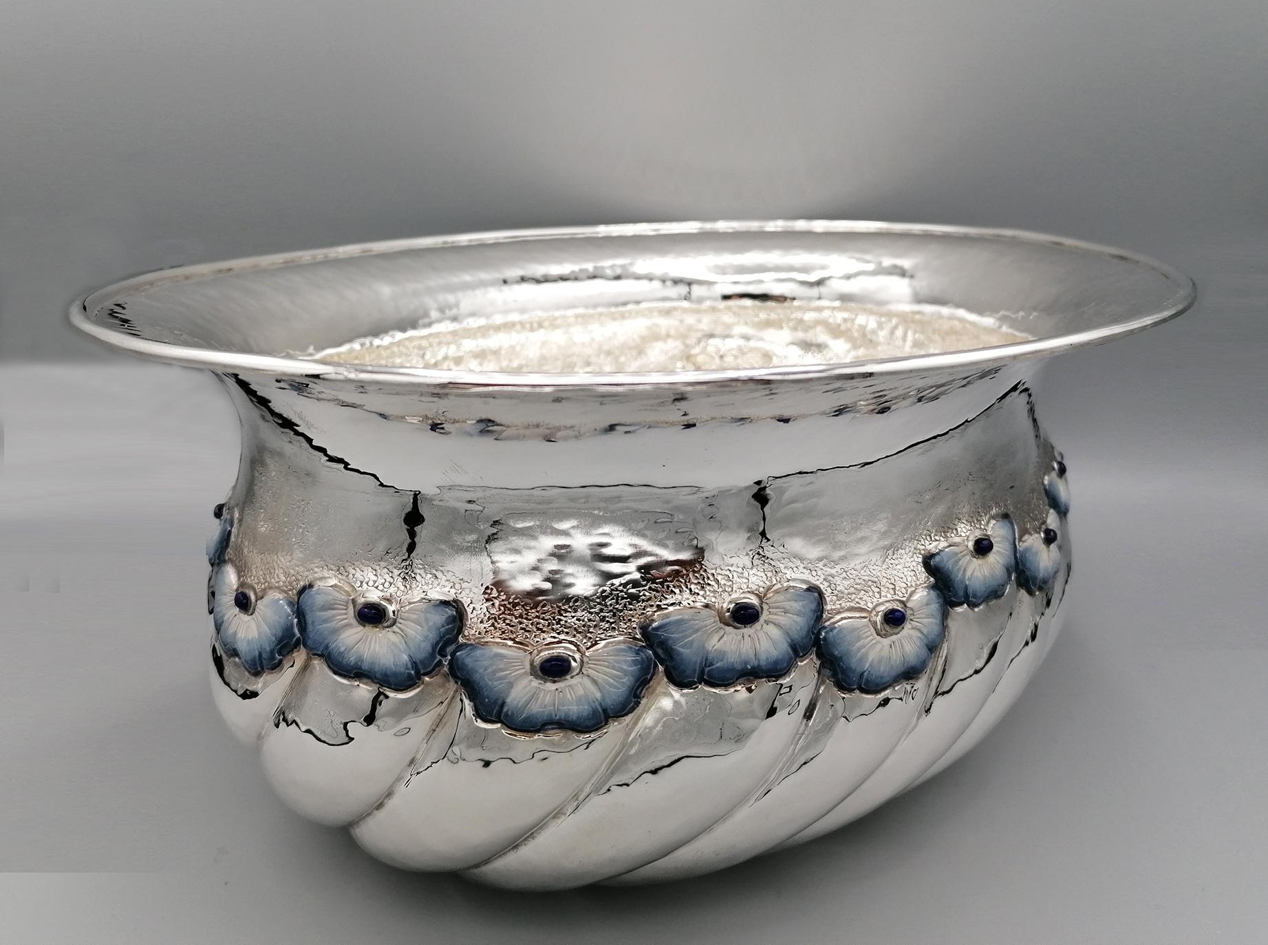 Oval centerpiece in sterling silver. The entirely handmade workmanship is embossed with a torchon design. In each sector of the torchon a flower was embossed and chiseled and subsequently enameled with fired enamels with the colors blue, light blue