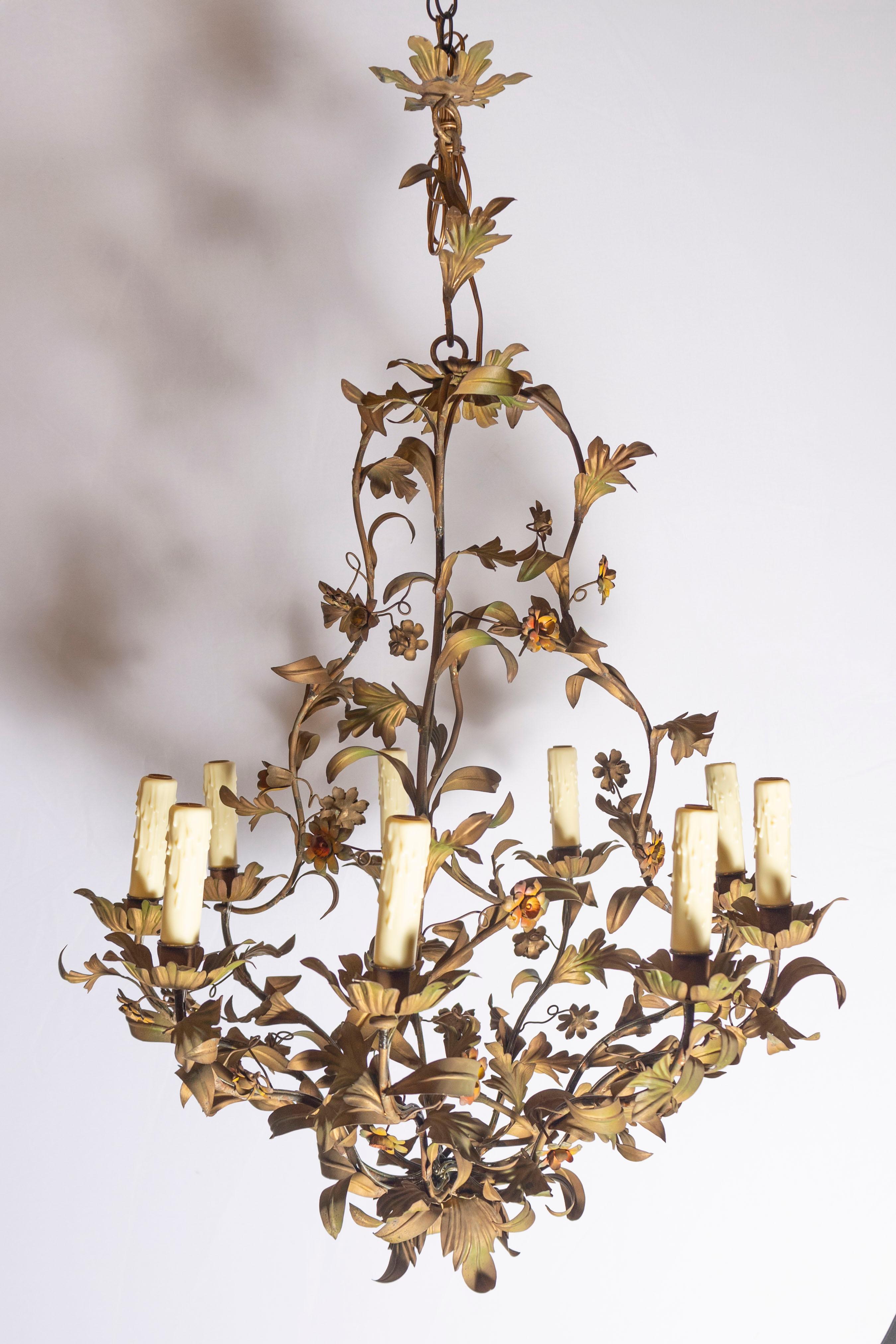 Débordant d'élégance botanique, ce lustre italien exubérant du milieu du XXe siècle capture le charme romantique de la nature en pleine floraison. Fabriqué à la main à partir de tole peint, ce lustre présente une composition luxuriante de lianes en