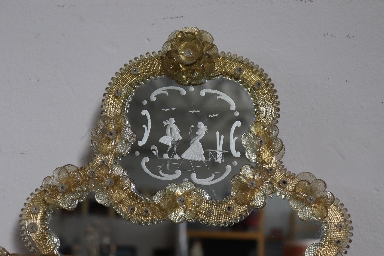 Beautiful elegant Italian Murano art glass wall mirror. Characterized by golden yellow decorative vegetal and floral glass elements. Rich decoration engraved in the mirror with a love scene between a young couple in the upper part. The artistic