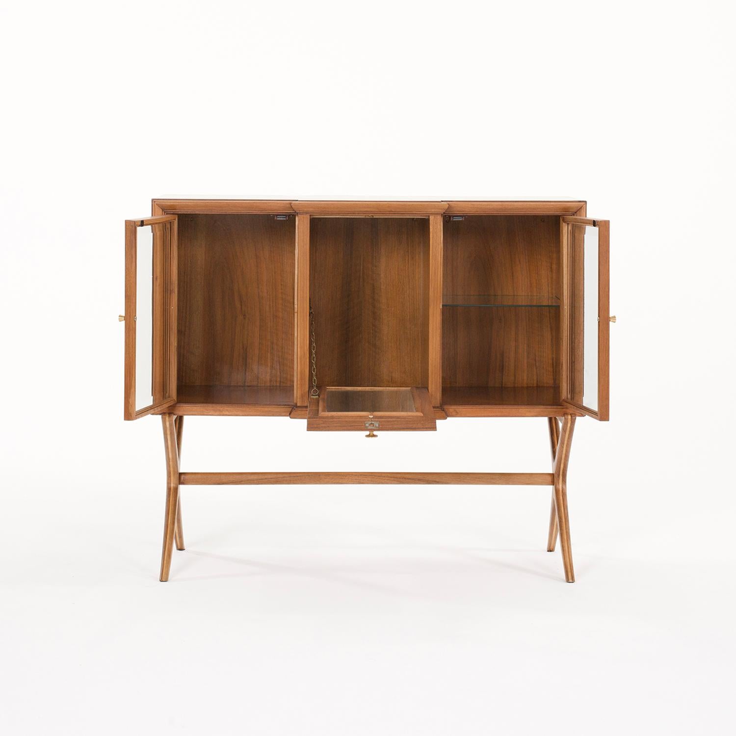 A small, vintage Mid-Century modern Italian cocktail dry bar made of hand crafted polished Walnut, in good condition. The vitrine cabinet is composed in the middle with one foldable door which is halted, enhanced by a brass chain. The sideboard is
