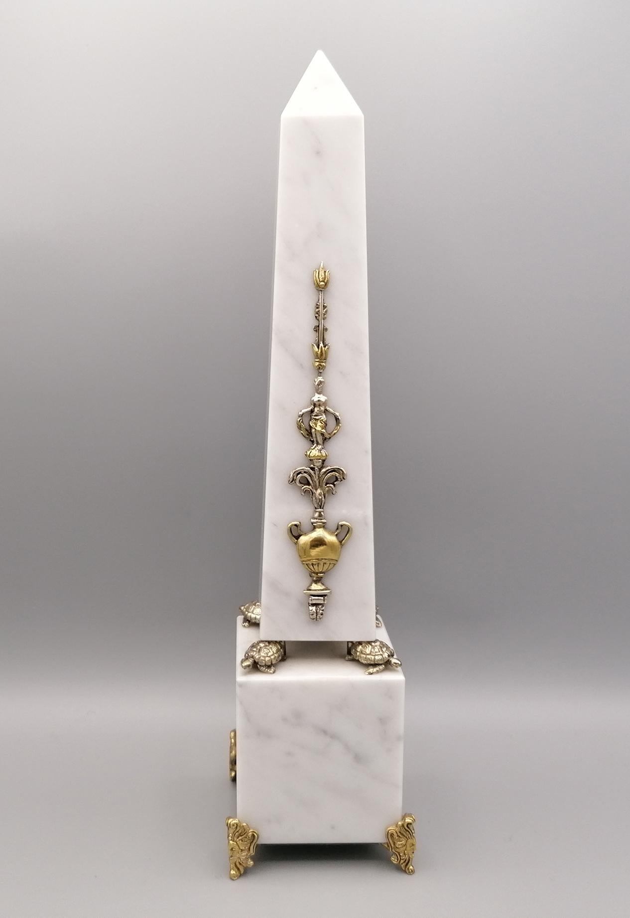 White Carrara marble obelisk with sterling silver friezes.
The obelisk frieze, in gilded and natural sterling silver, depicts a jug from which water flows at the feet of a woman and is placed on a base, also in white marble, on 4 turtles in 925