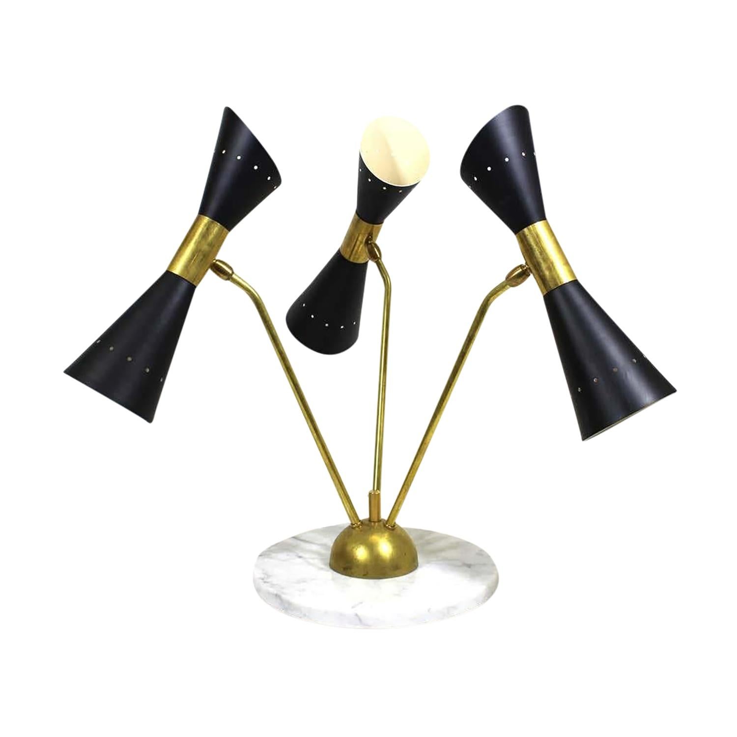 Lampada da tavolo o da scrivania vintage Mid-Century Modern in metallo e ottone lavorato a mano, nello stile di Stilnovo, in buone condizioni. I tre paralumi a montatura conica, in metallo laccato nero traforato, sono sostenuti da bracci in ottone