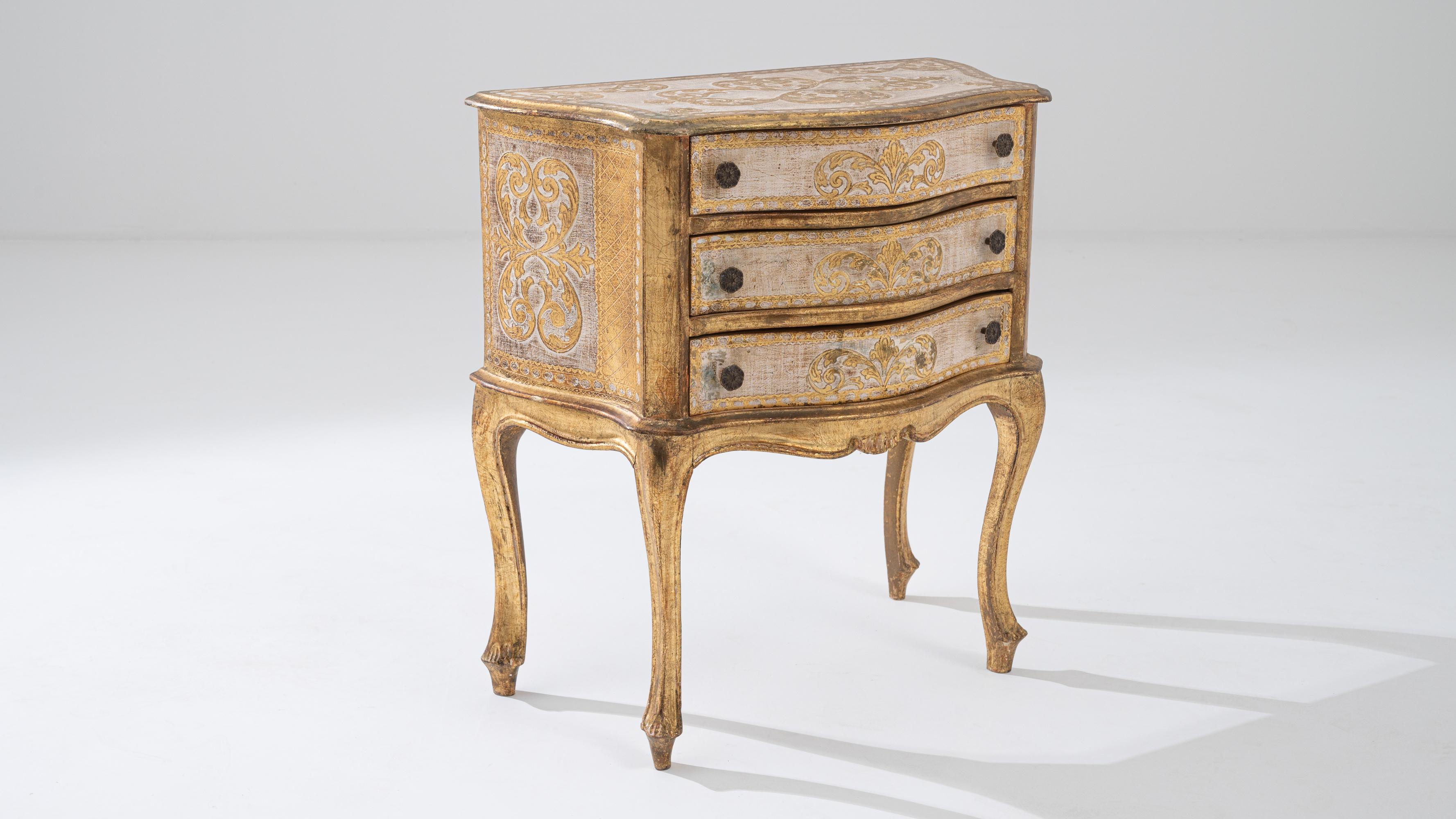 Immerse yourself in the timeless allure of the Renaissance Era with this opulent 20th Century Italian Wood Patinated Chest of Drawers. Boasting luxurious gold and cream tones, this vintage chest is a masterpiece of design. The intricate scrollwork