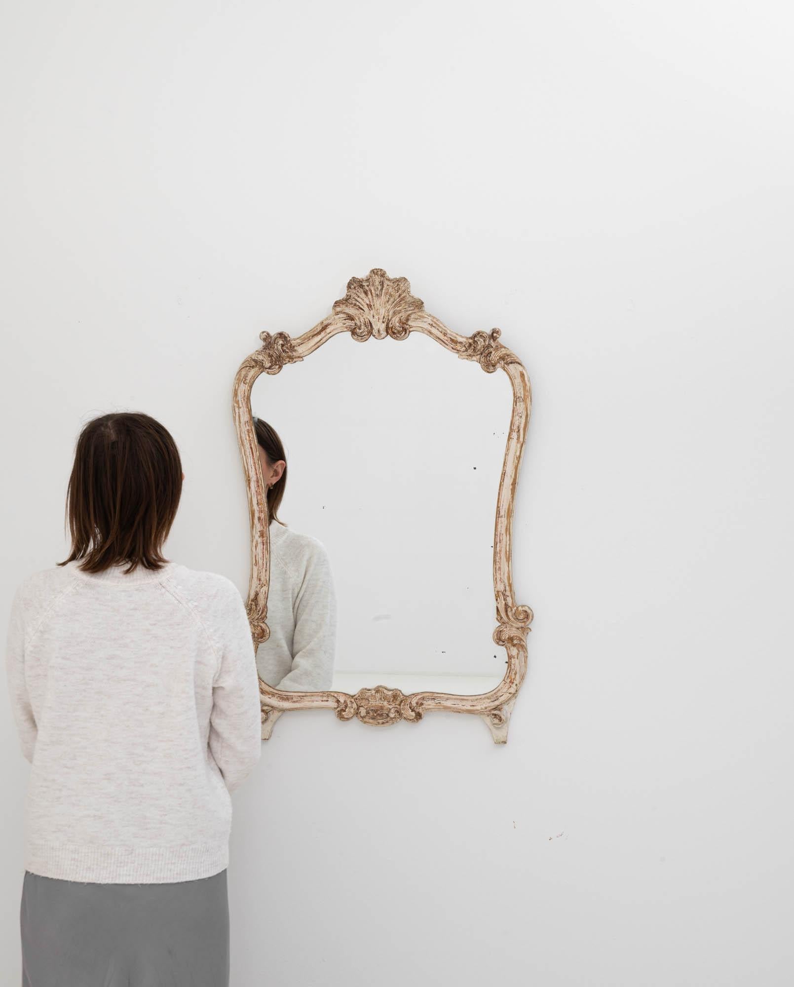 Step into a world where the elegance of the 20th century Italian design meets the rustic charm of a time-worn treasure with this exquisite white patinated wood mirror. The curvaceous silhouette is accentuated by ornate carvings that flourish at the