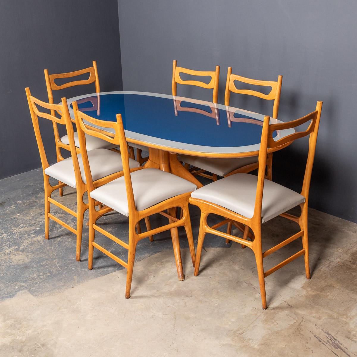 Modern 20th Century Italian beech table on a spreading four leg pedestal accompanied by a set of six complimentary chairs made of lacquered light wood, leather covered seats and glass covered table top, presented at the Brussels exposition