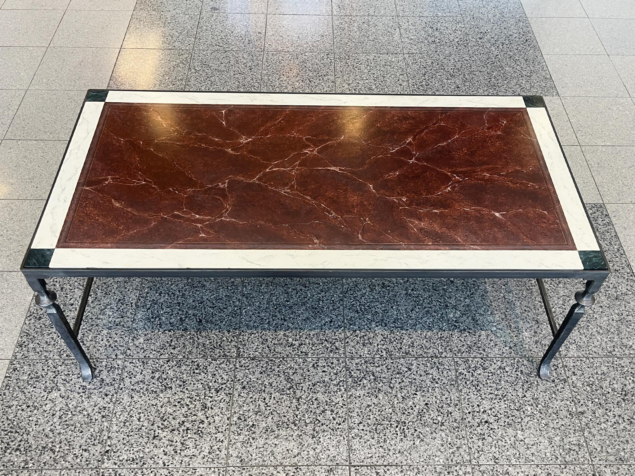 Fabriquée à la main en Italie, cette table basse a une base en fer forgé et un plateau en faux marbre. Le faux marbre a une sensibilité néoclassique, avec son champ central rouge sang de bœuf et une bordure composée de blanc et de vert émeraude. La