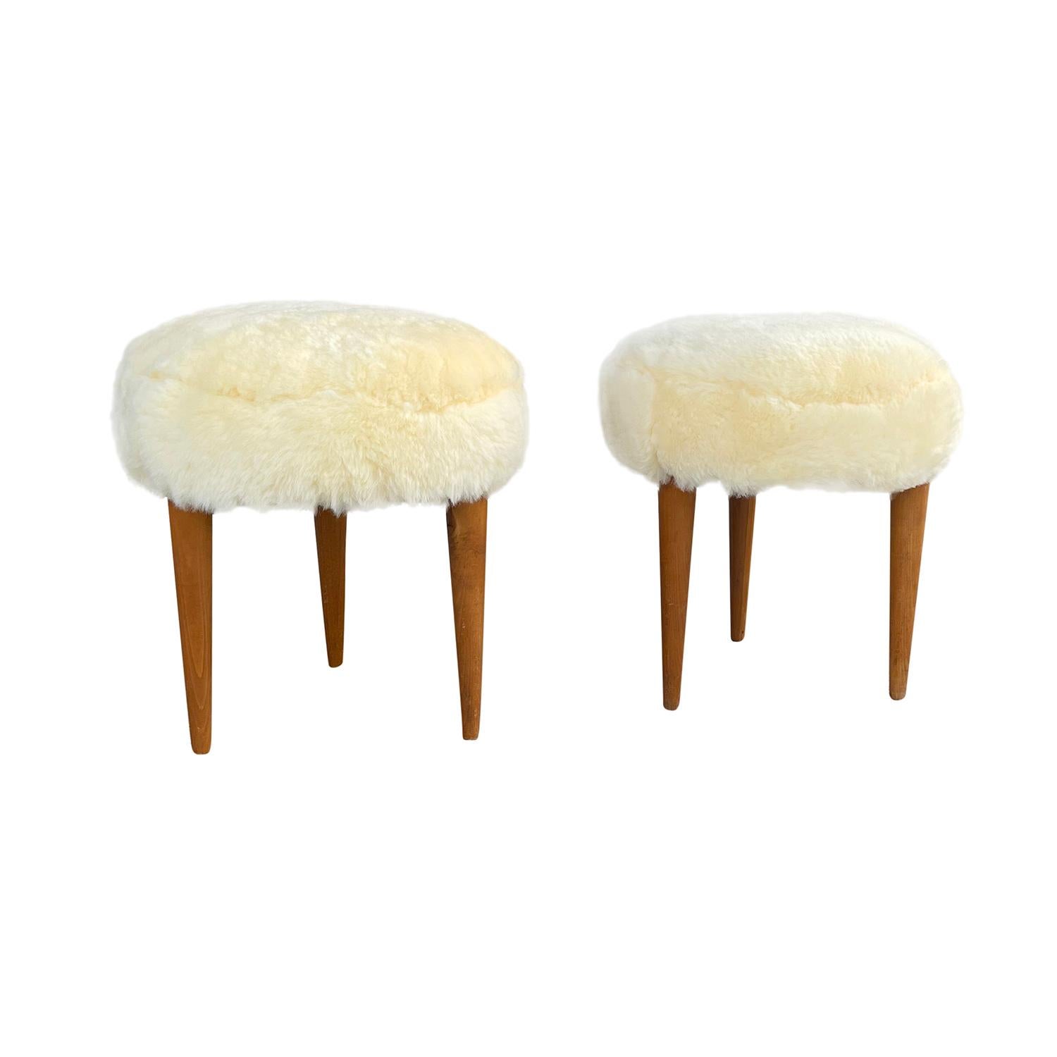 A vintage pair of Mid-Century Modern Italian round stools made of hand crafted walnut, standing on three straight wooden feet, in good condition. Newly upholstered in yellow sheepskin. Wear consistent with age and use, circa 1950-1960, Italy.