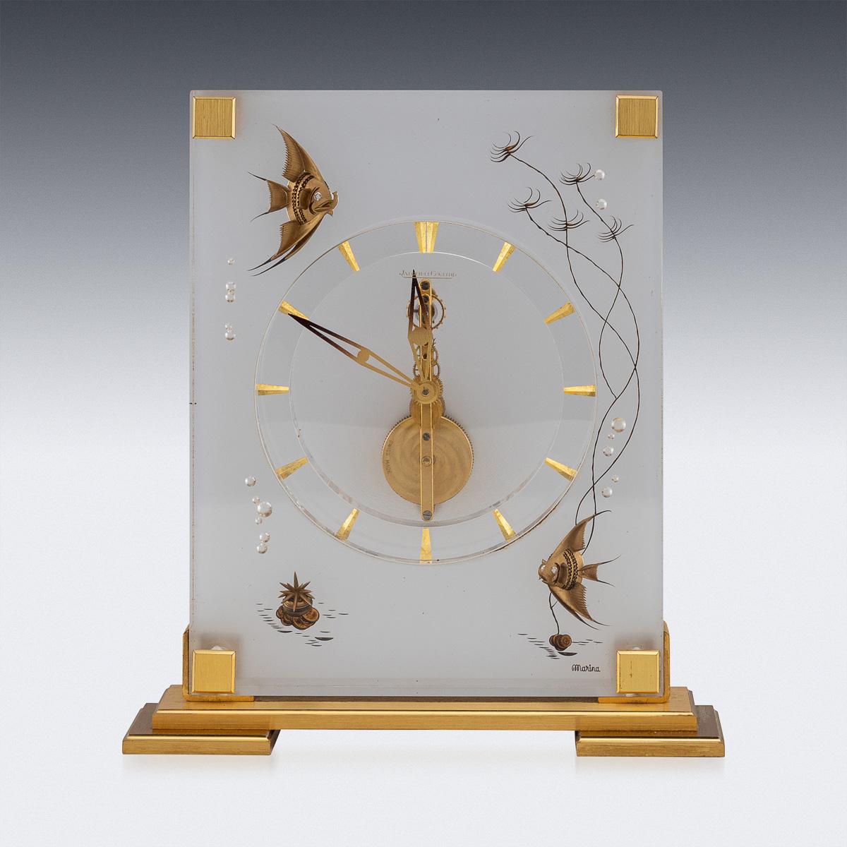 A Mid-Century mantel clock by Jaeger-LeCoultre graces its surroundings with an elegant Lucite case adorned with inset brass decorations depicting fish among reeds and rising air bubbles. It operates on an eight-day movement, featuring