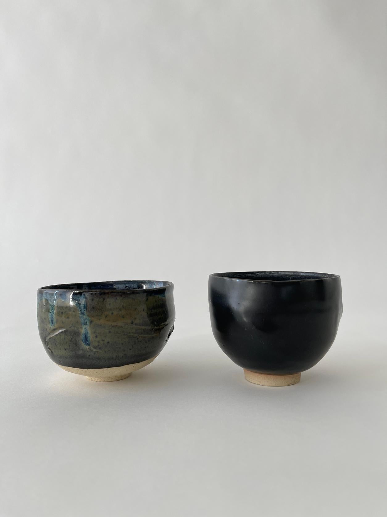 20th century Japanese Ceramic tea cup set with an abstract form and dark colored semi glazed body with textured off white bottoms. 

Set of 2
Measures: Cup 1: 4