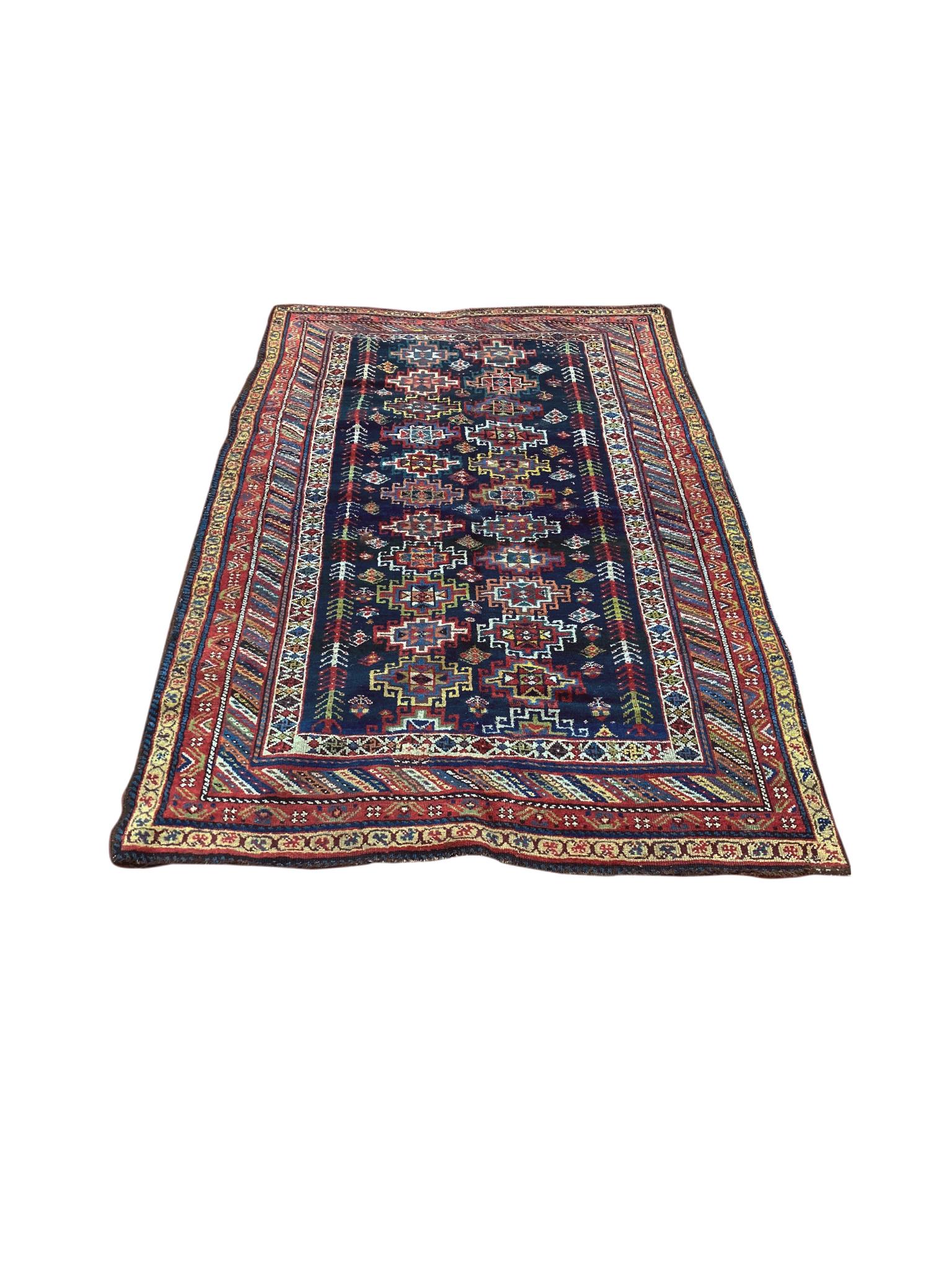 A vintage Kurdish area rug with a rich palette of blues, yellows, and reds that are beautifully arranged into medallion motifs and geometric bands. The center field is a dark navy blue with two parallel rows of medallions and buta motifs. A series