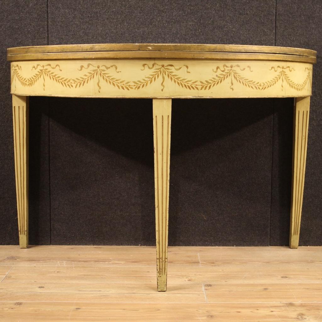 Italian demilune table from the first half of the 20th century. Furniture of beautiful line and pleasant decor in Louis XVI style in carved, lacquered and hand painted wood with floral decorations. Opening table which, once opened, reaches a