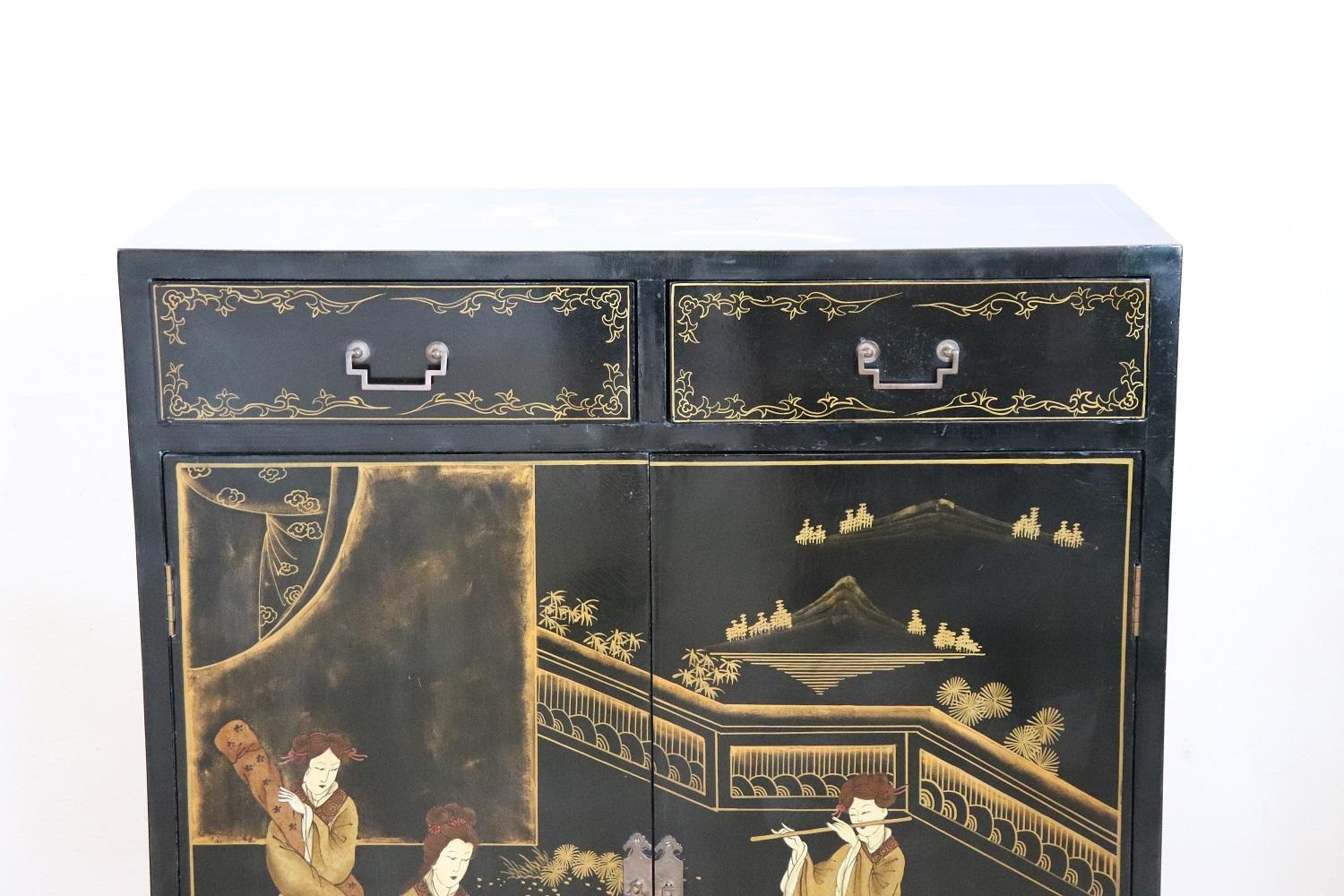 French beautiful small cabinet 1960s. Made of black lacquered wood, refined hand painted gold decorations in japanese style. On the front doors there is a beautiful animated scene with young geishas playing musical instruments. On the sides flowers