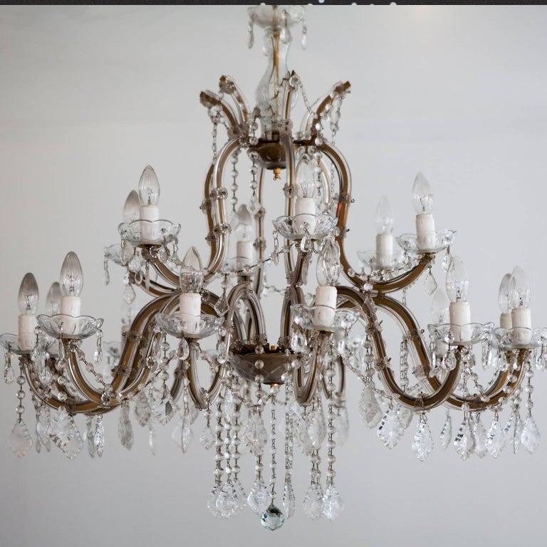 A French gilded brass and cut-glass two-tier eighteen-light antique chandelier, scrolling arms with sectional leaf drip pans, issuing from a cast central column with canopy and decorated overall with faceted cut pendants with chain and ceiling rose,