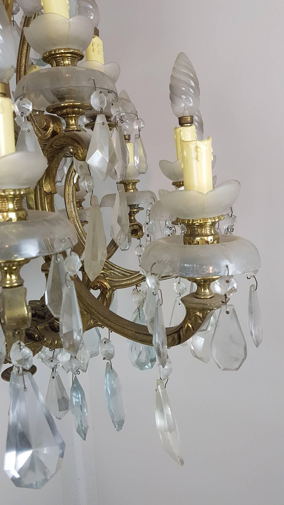 20th century beautiful and elegant chandelier 18 lights golden bronze and crystals circa 1920s. The bronze is richly worked and finished in details even the drops are finely worked gives it an elegant gloss. The 18 light bulbs are arranged in two