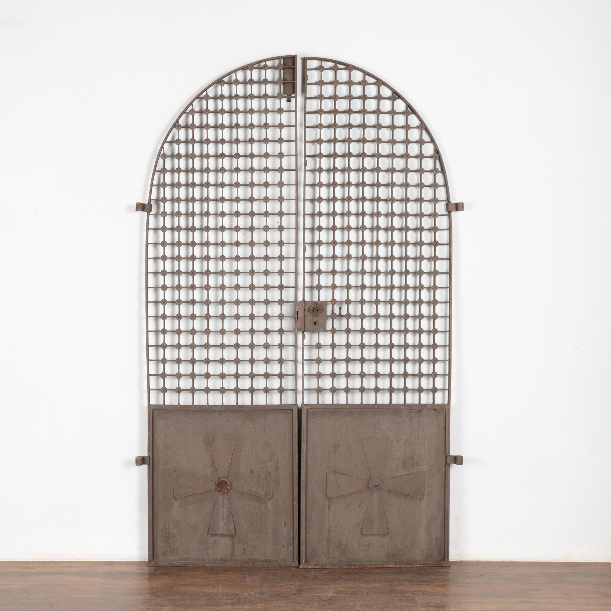 This large pair of arched iron doors make an impressive architectural statement standing just over 8' tall.
Notice the inviting upper open lattice work and lower solid panel with cross pattern.
The aged patina shows rust and wear which add to the