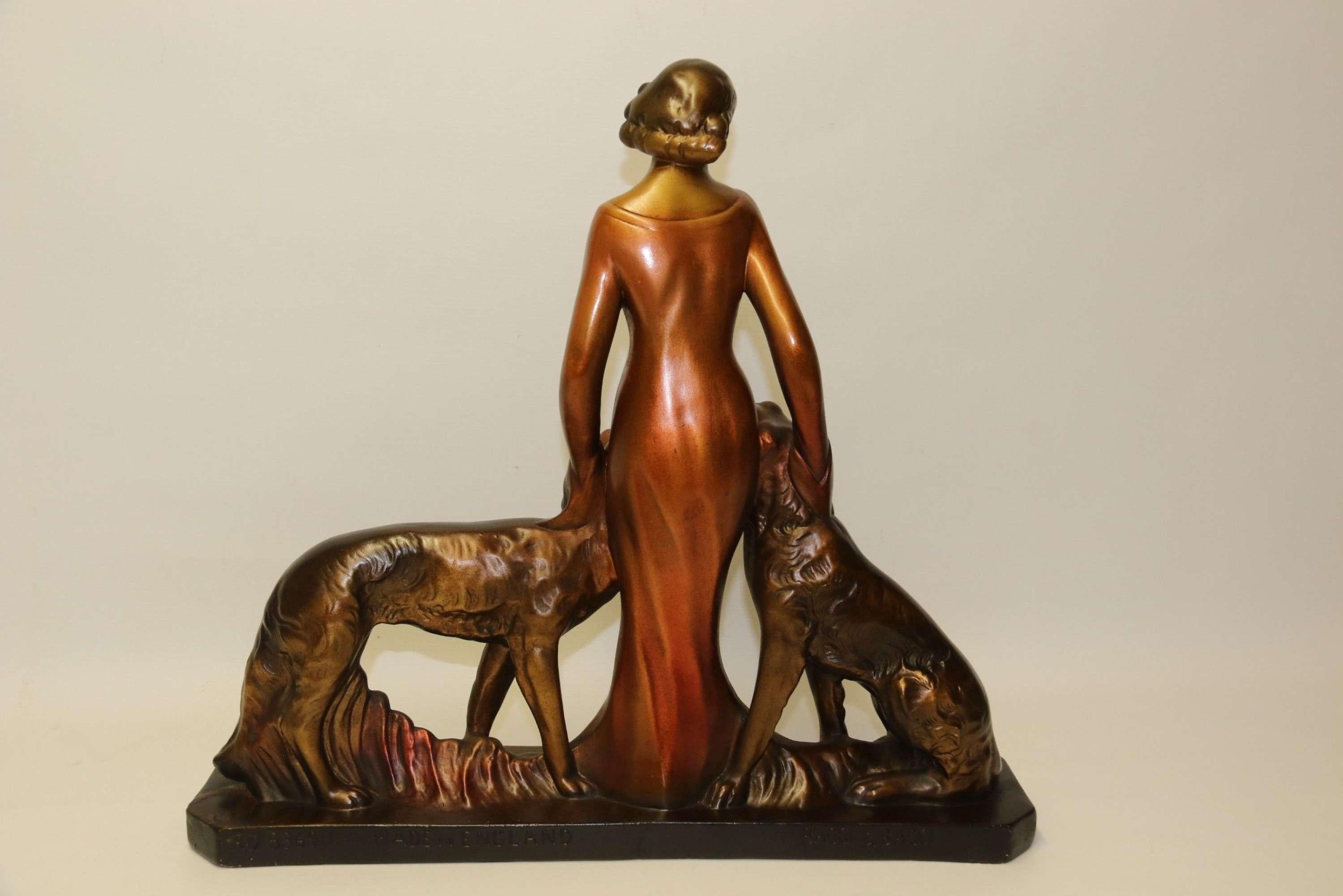 A Large Art Deco English Figure Group

This large and highly decorative 1930s figure group depicts a beautiful young woman dressed in an evening gown standing elegantly with her two Russian Borzoi dogs. It is made from plaster and cold painted in