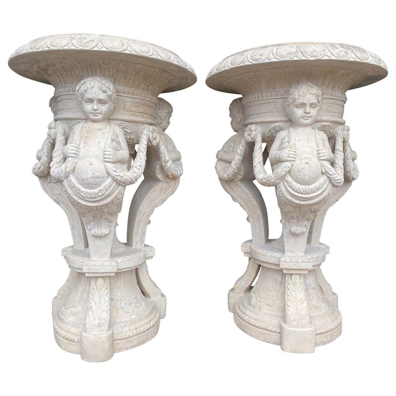 A stunning 20th century large pair of hand carved marble planters. Decorated with cherubs and swags of foliage with egg-and-dart moulding to the rim. Sat on circular bases this pair have astounding presence. Perfect as garden ornaments and home