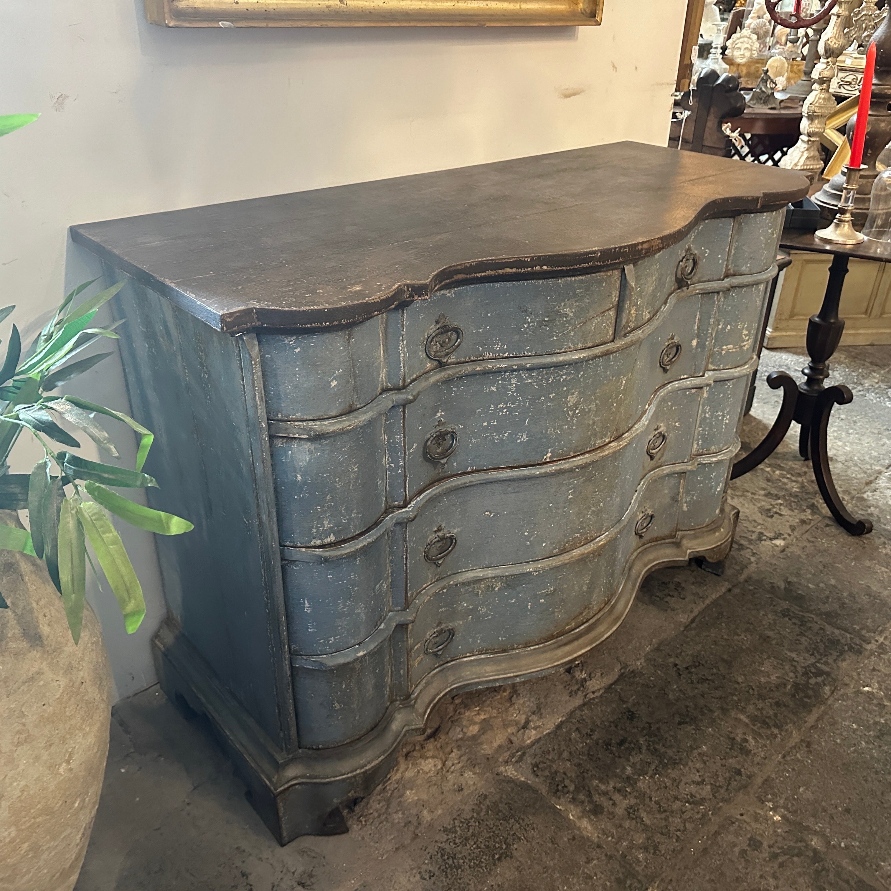 This is a 20th-century chest of drawers styled in the Louis Philippe tradition, featuring a lacquered blue and black finish with a Tuscan flair. The piece has an elegant serpentine front, a hallmark of Louis Philippe design, with soft, flowing