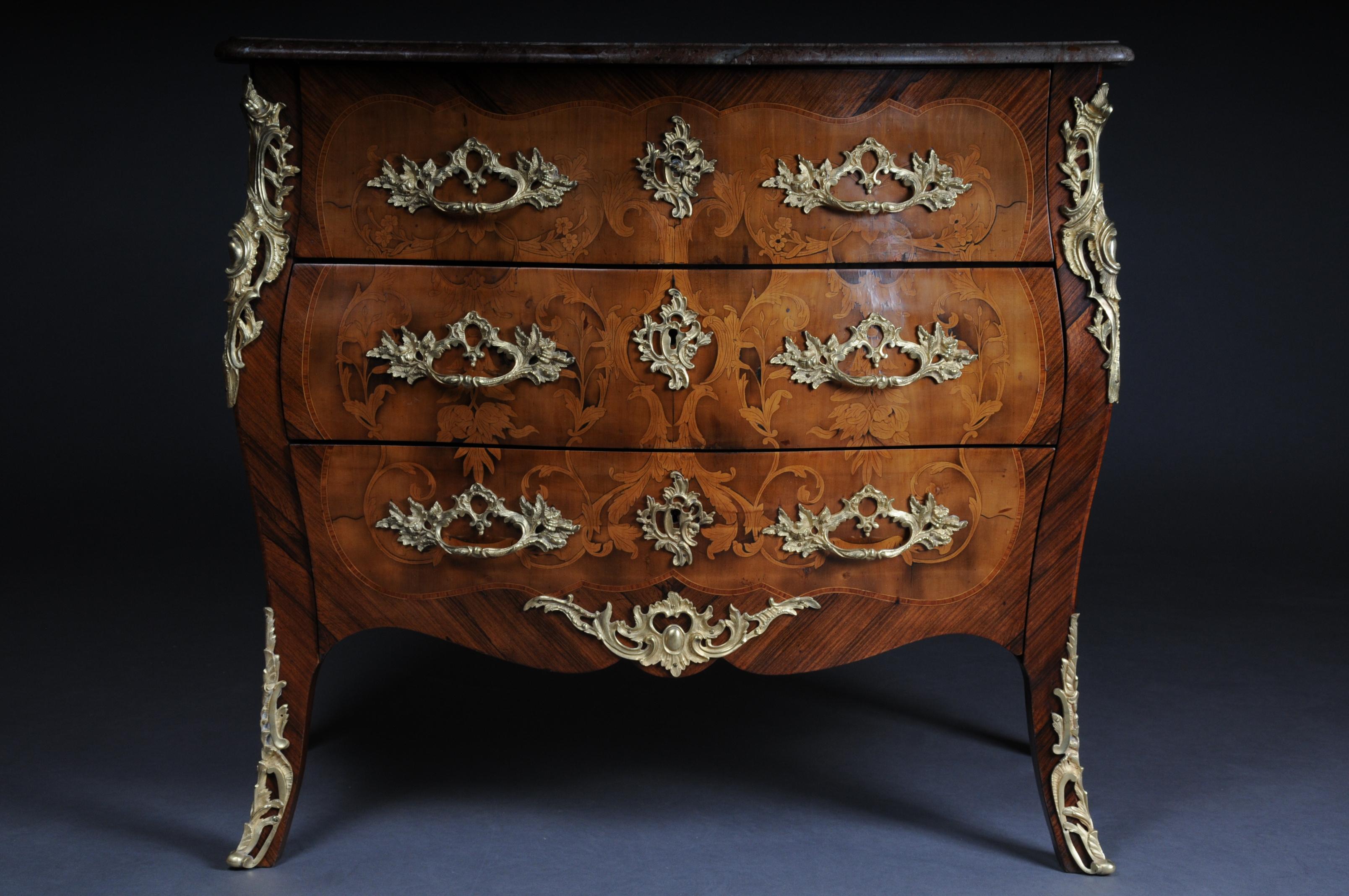 Louis XV style chest of drawers
Tulipwood veneer and maple. Body cambered on all sides with protruding corners. On both sides and front over the three drawers, market decorations made of acanthus volutes, rocaille and flower curtains. Fire-gilt