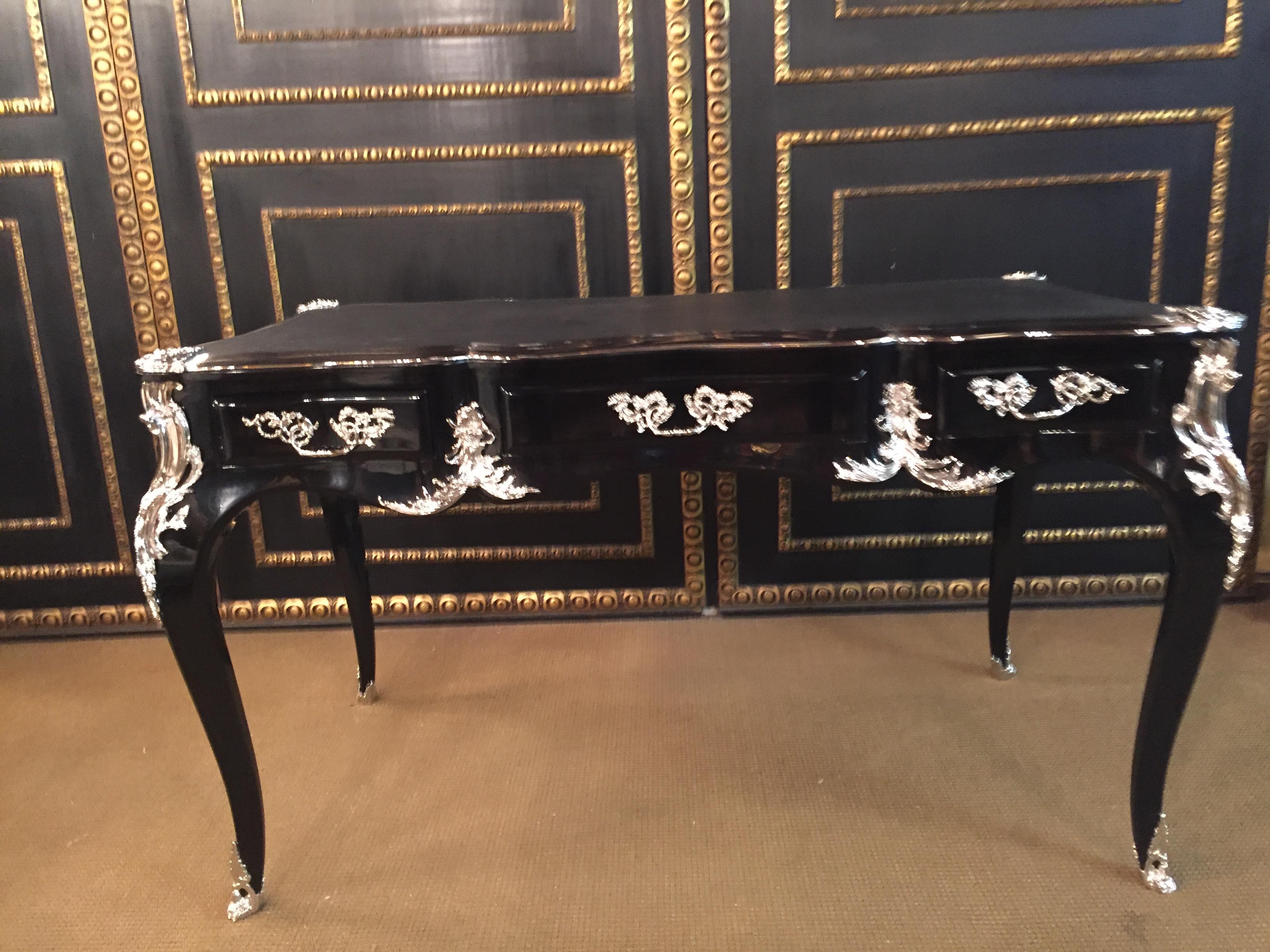 Bureau plat writing table in the style of Louis XV style, silvered bronze fittings. Piano lacquer black on solid beech wood. Heavily arched, four-sided passively curved tripod frame with wide knee lug on elegant curved squares in the drive boxes.