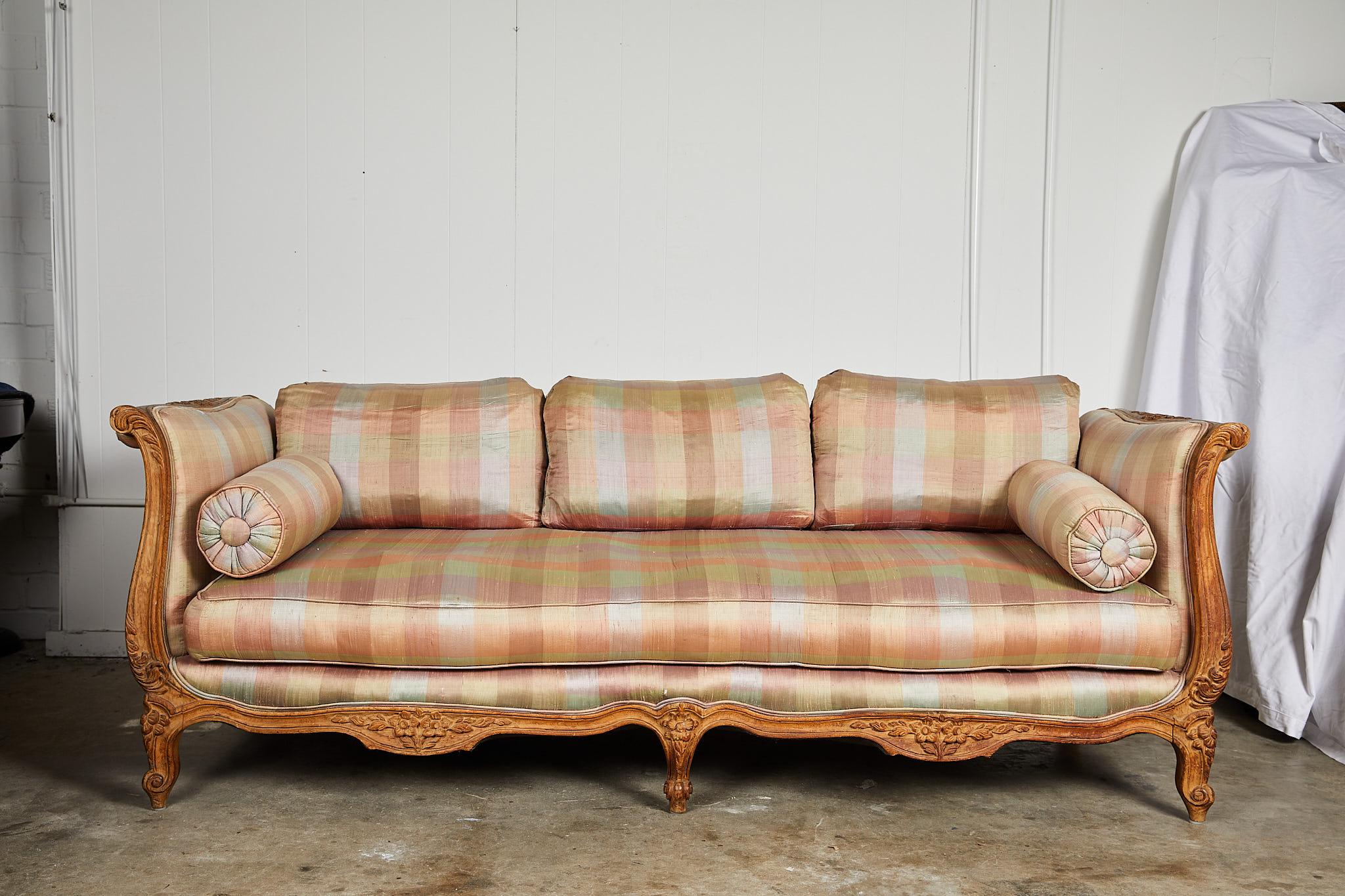 20th century Hollywood Regency sofa or daybed influenced by the French Louis XV aesthetic featuring a pickled and carved wood frame and upholstered in a striped silk. The generously proportioned sofa frame and down blend cushions are in great