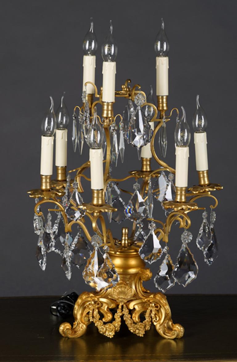 Exclusive Girandole in the Louis Quinze style. Brass, chiselled. On three-legged curved plinth with three flared feet with garland trim. High baluster-shaped body. Outgoing nine passively flared luminaries. In three further graded levels bent