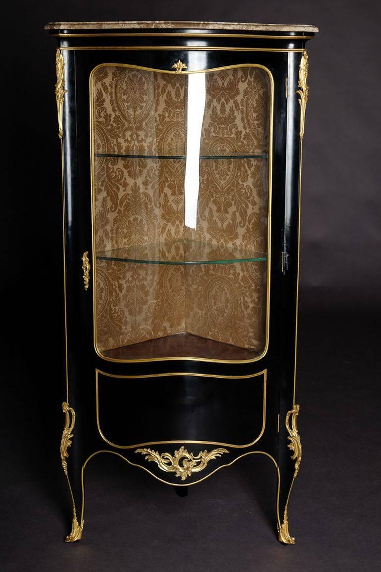 Petite Französisch Vitrine im Stil von Louis XV Rokoko
Klavierschwarzes, poliertes Furnier auf massiver Buche. Hoch aufgerichteter, einarmiger, gewölbter Körper, dreiseitig bis dreiteilig, auf hohen, schräg gestellten, gelockten Füßen. Profiliertes