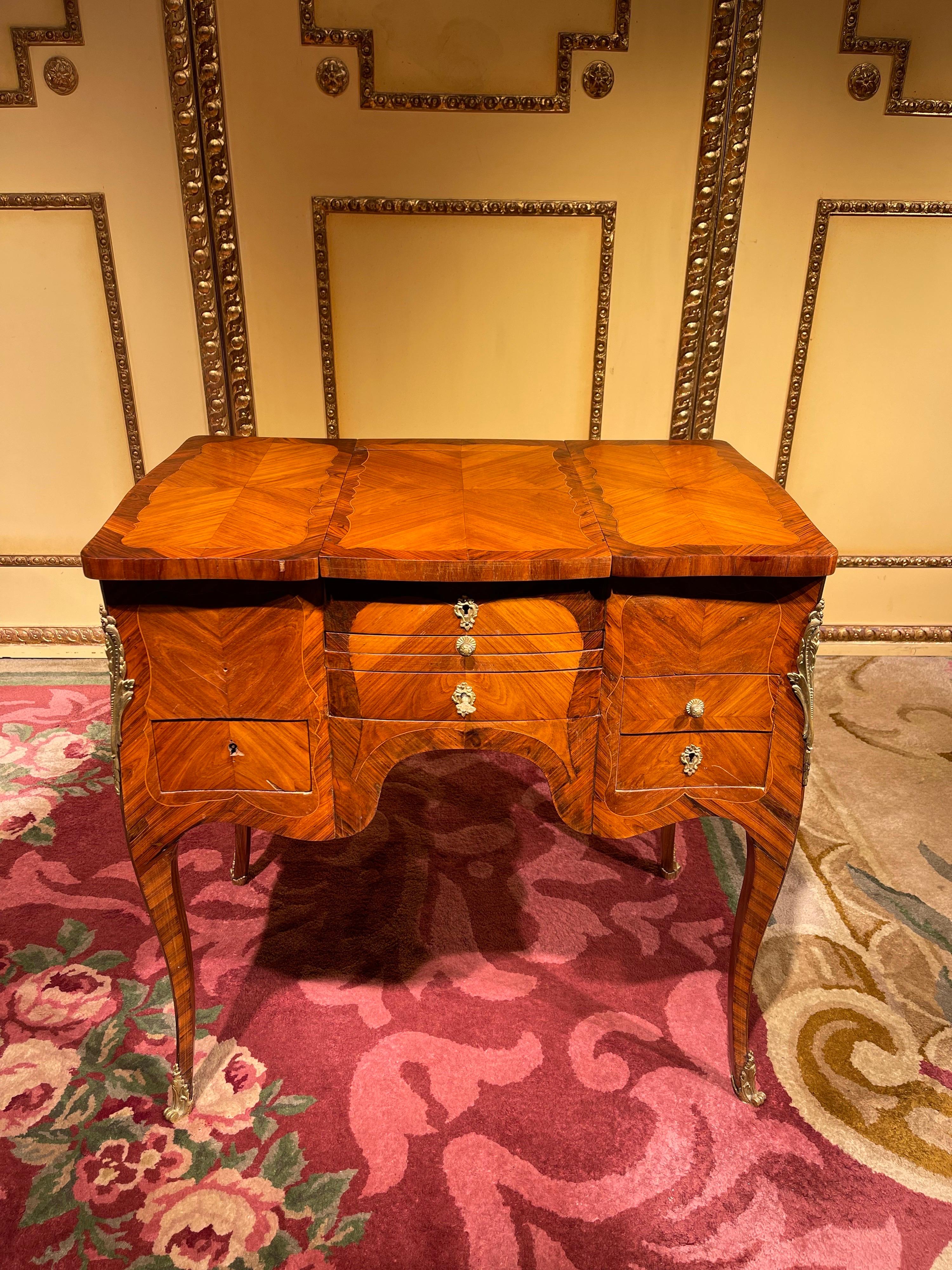 Fine wood veneer with thread inlays and decorative brass fittings. Curved cover plate with hinged middle part, inside with mirror. Four-drawer body with sideboard, on graceful, curved legs. Brass key covers and handles. Locks with keys available.