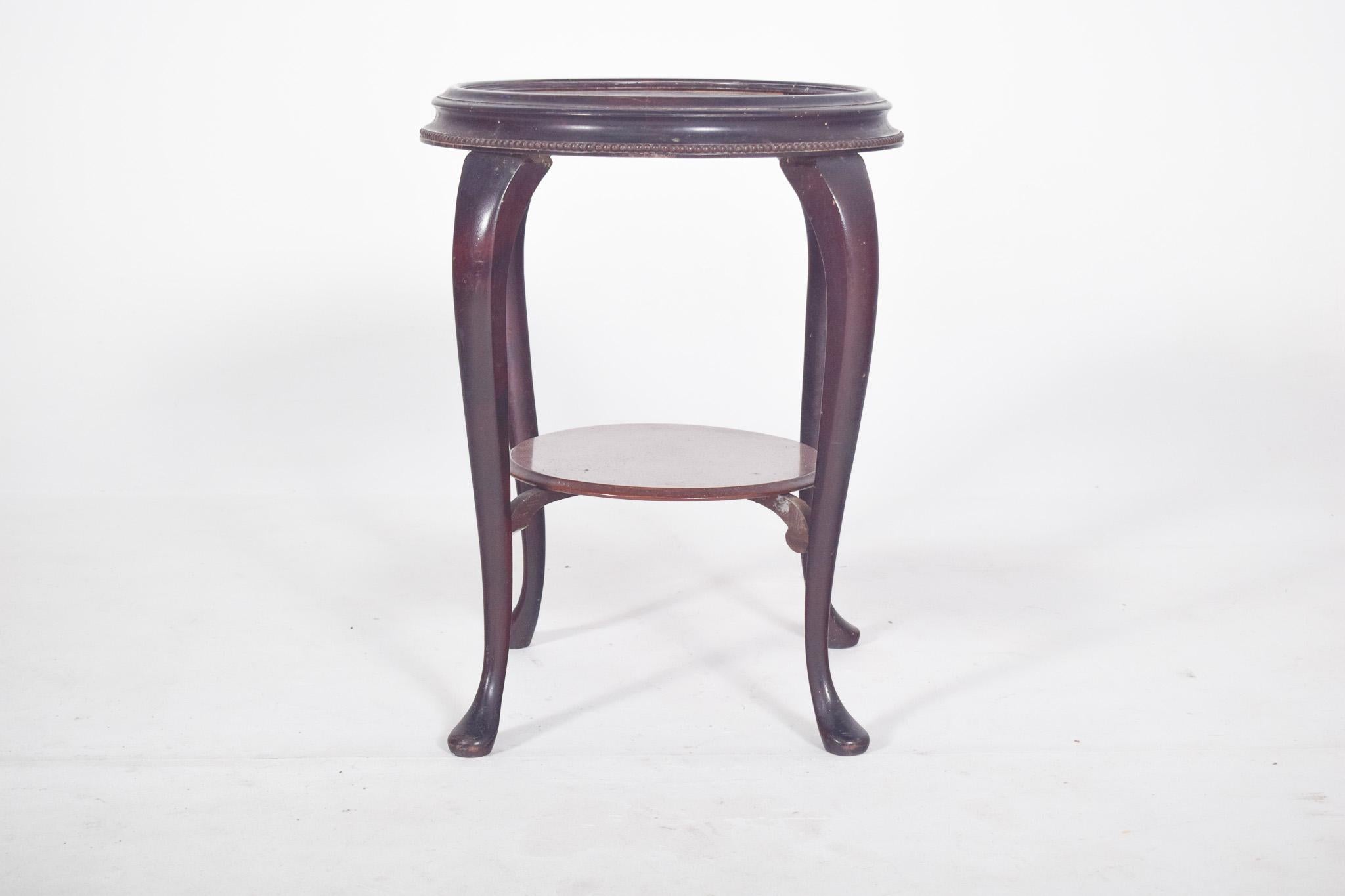 Tavolino rotondo. In legno tornito e piano in marmo, circondato da un bordo curvo con fregio intagliato in basso. Le gambe sono ricurve, si allungano dolcemente verso il pavimento e presentano dei semplici terminali. 
Nella parte inferiore, un