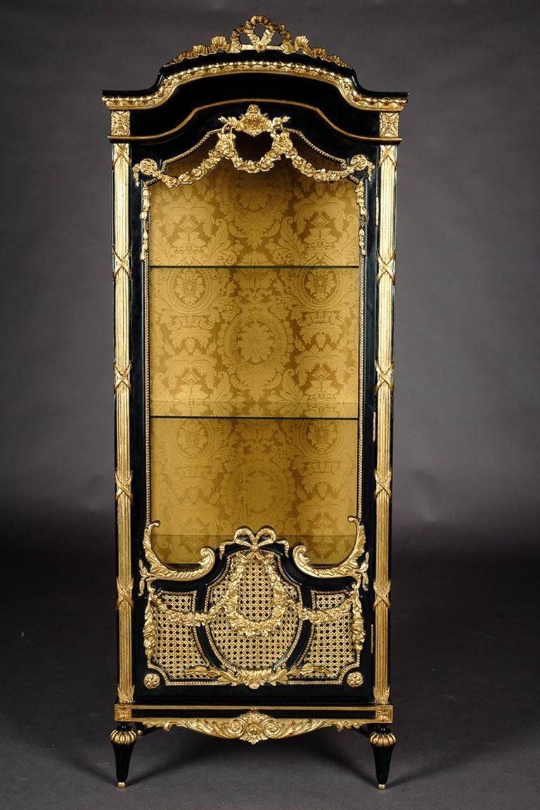 Black piano veneer on solid beech, gilded, ebonized. The front, corners and sides are applied with carved, classicist elements such as garlands and beveling. Elaborate carvings, broken crowning. 

(O-Sam-173).