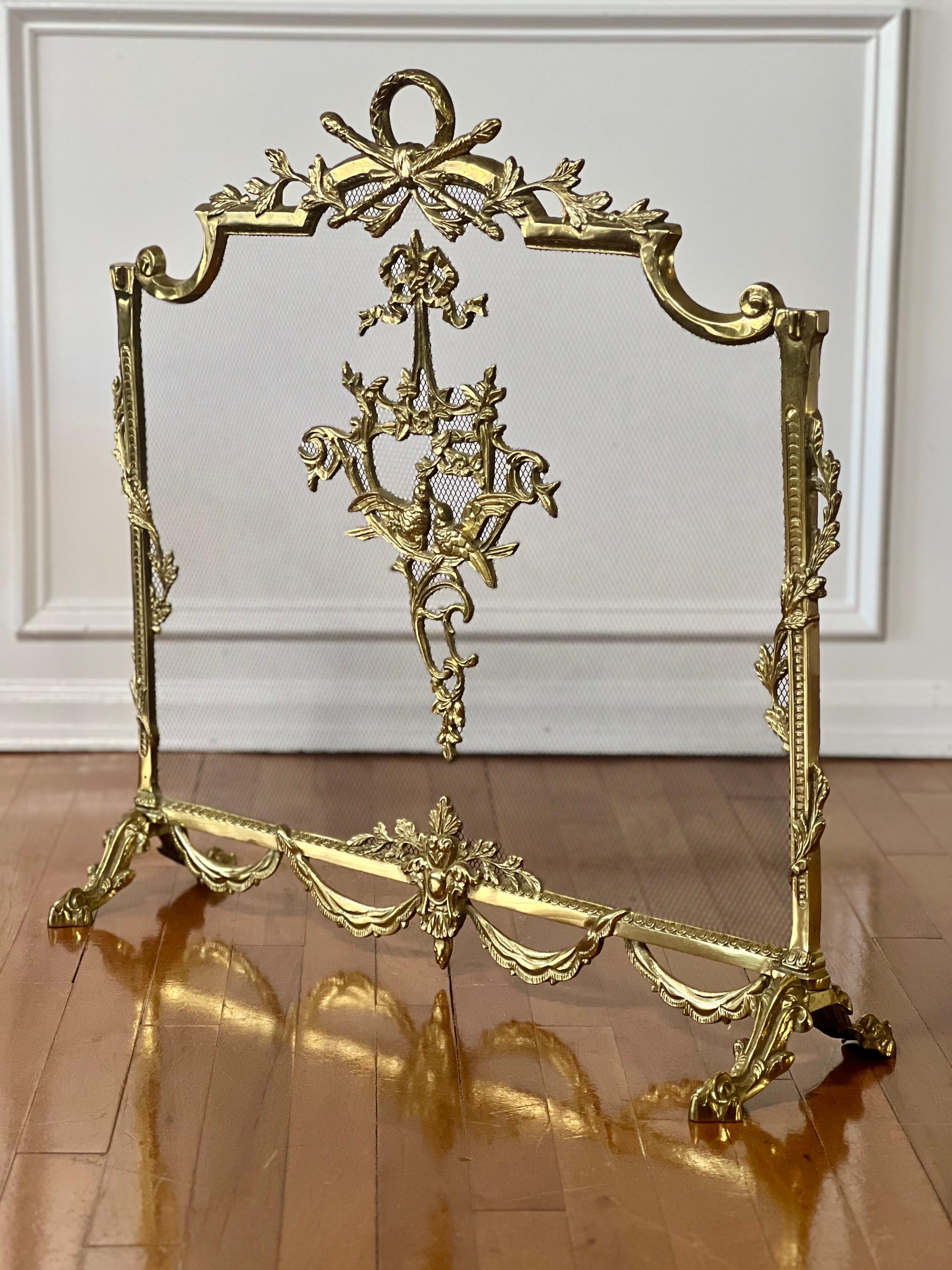 20th century Louis XVI style brass fireplace screen. It is adorned with a central medallion with a pair of doves surrounded by scrolling acanthus leaves and flowers topped with a bow. Full of ornamental detail throughout with a laurel design forming