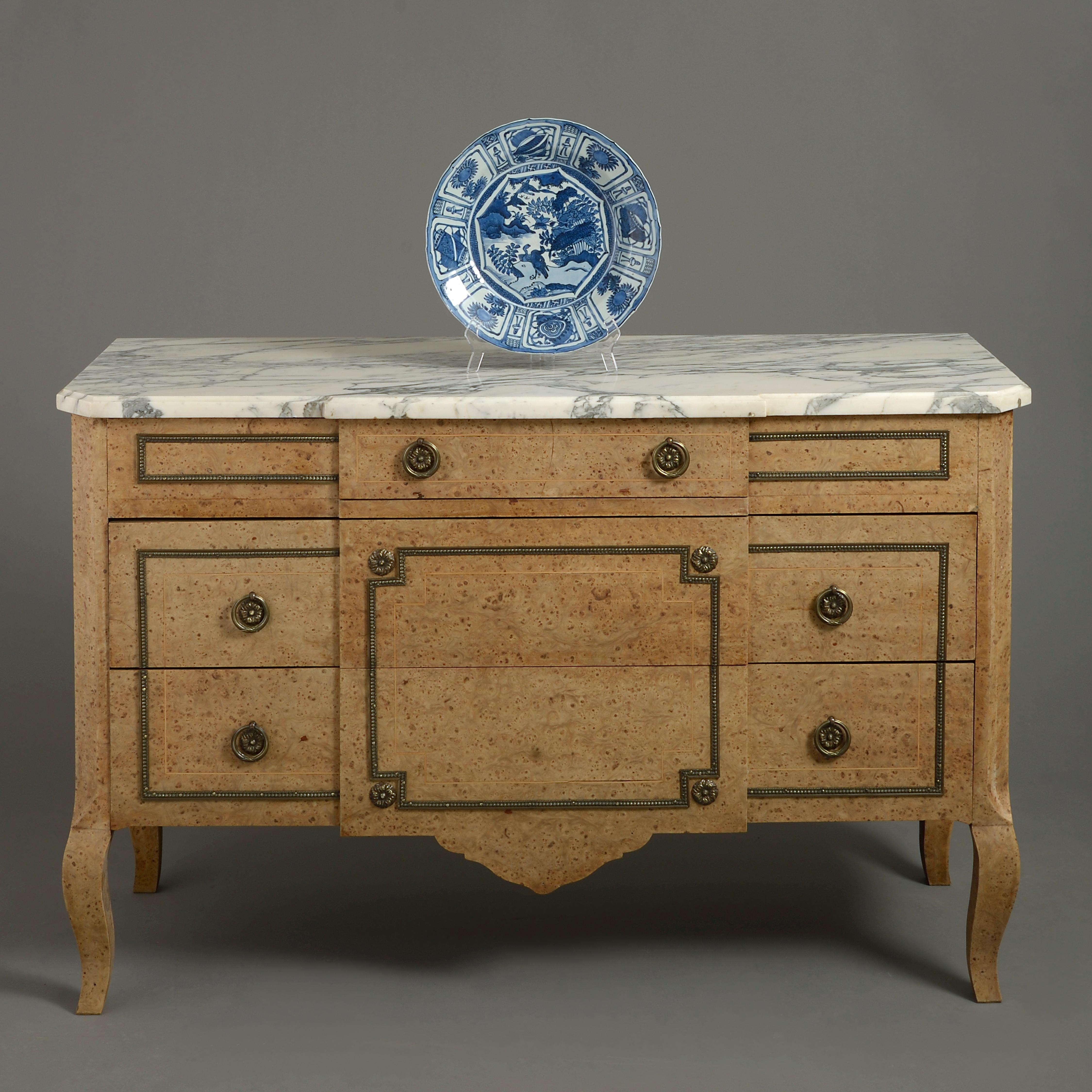 A mid-20th century burr elm commode, having a white marble top above three drawers with brass mounts and raised on shaped legs.