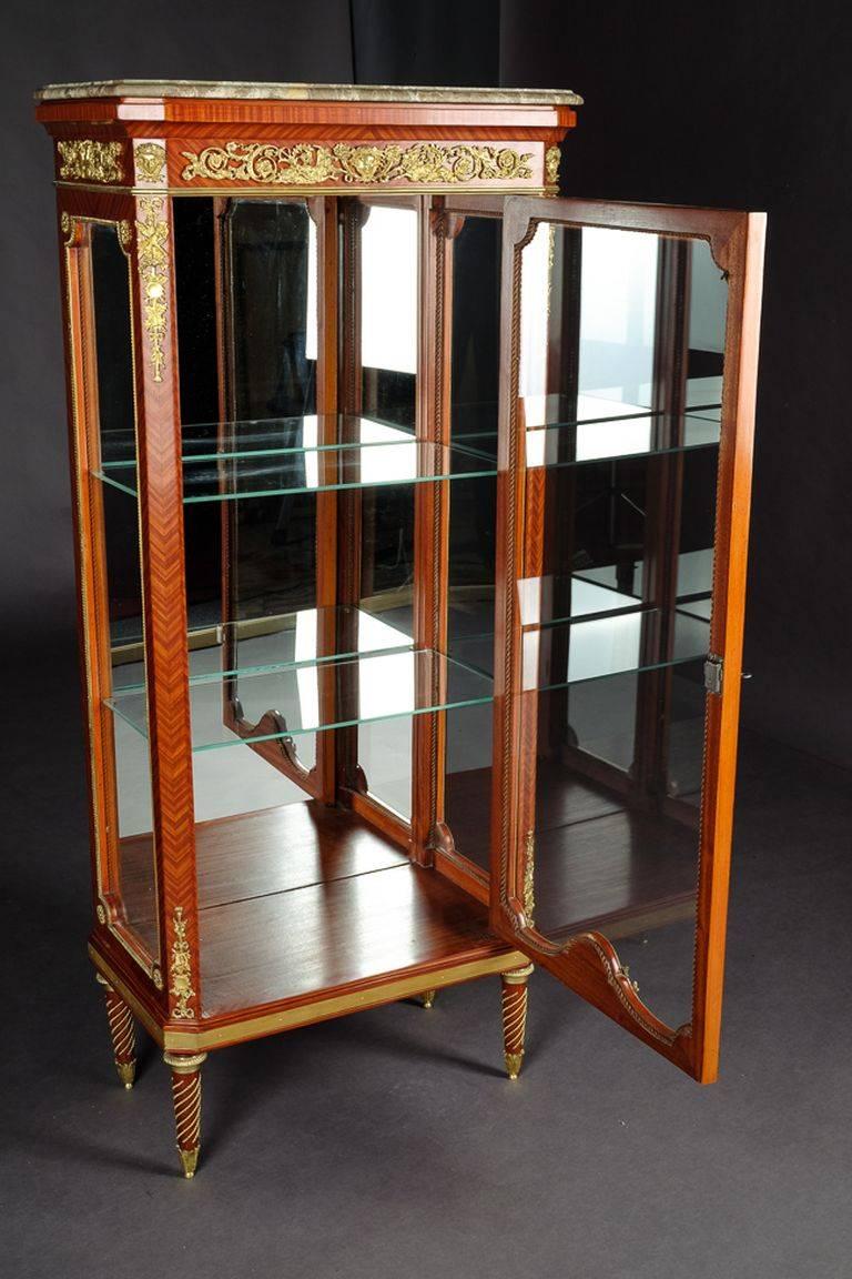 Exclusive French vitrine in Louis XVI style.
Finely engraved and moulded Bronze. Solid beechwood. Three sided glassed, one- drawered body on conical legs. Profile- framed flecked Marble platter. On the front, corners and sides, classicist